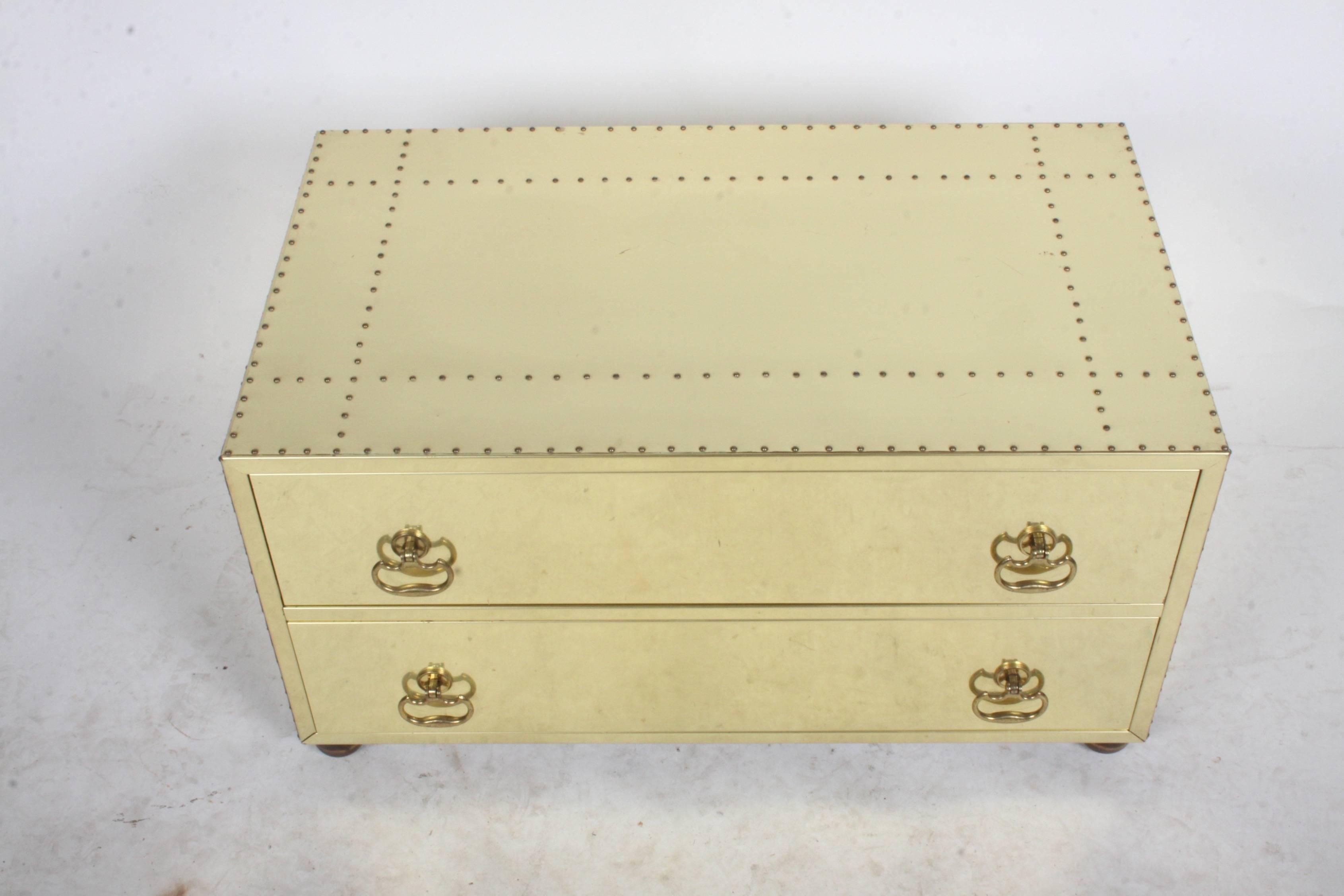 Brass clad studded chest in the style of Sarreid, circa 1970s or early 1980s. Two-drawer chest on bun ball wood feet. Minor scuffs and a ding, expected with age. Compliments Mastercraft Furniture. Please note very reflective, shows dirt from paper