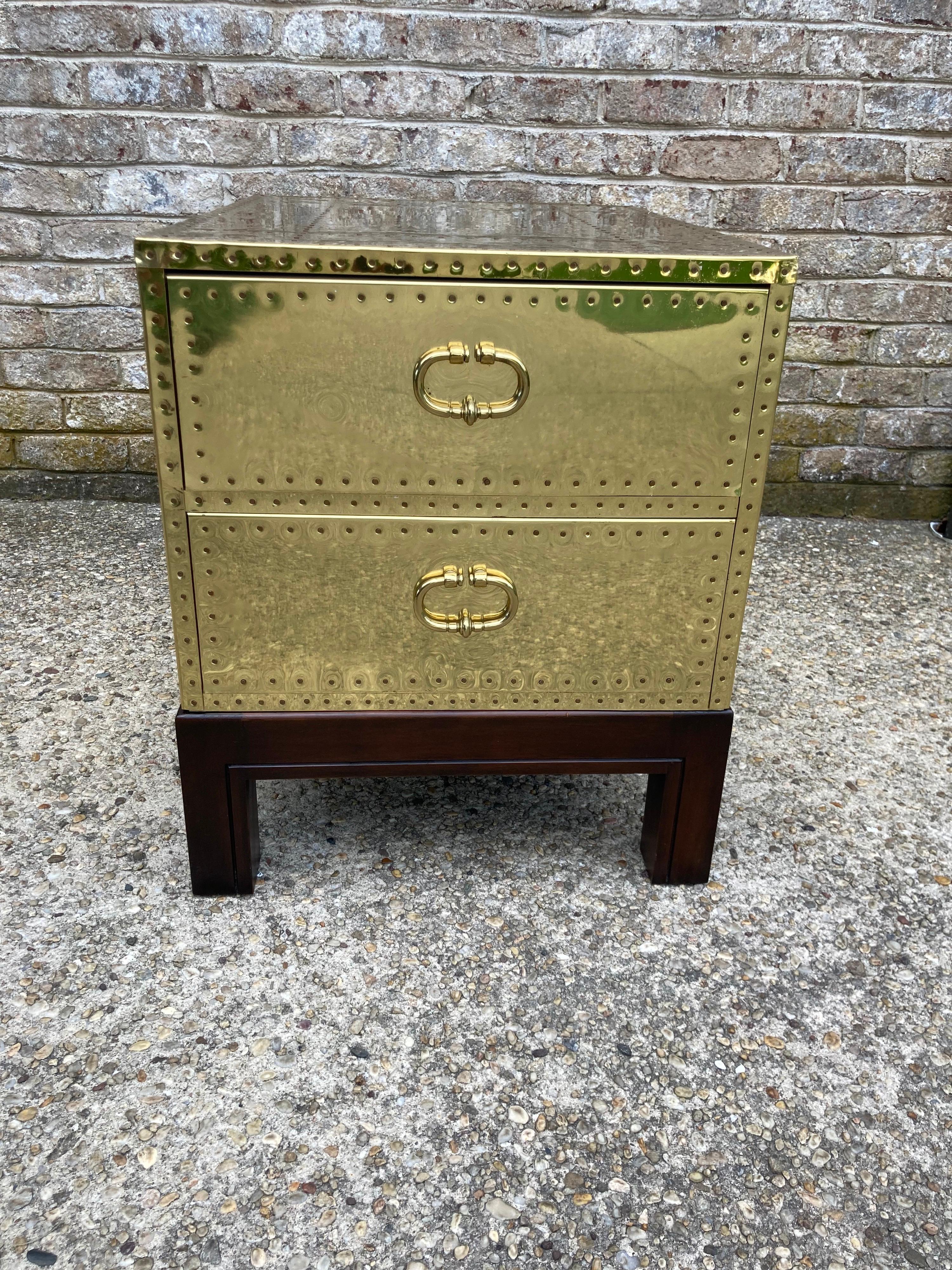 Pair of brass chests studded with nail heads with two draws. Made by Sarreid. Chests sit on a dark wood stands.