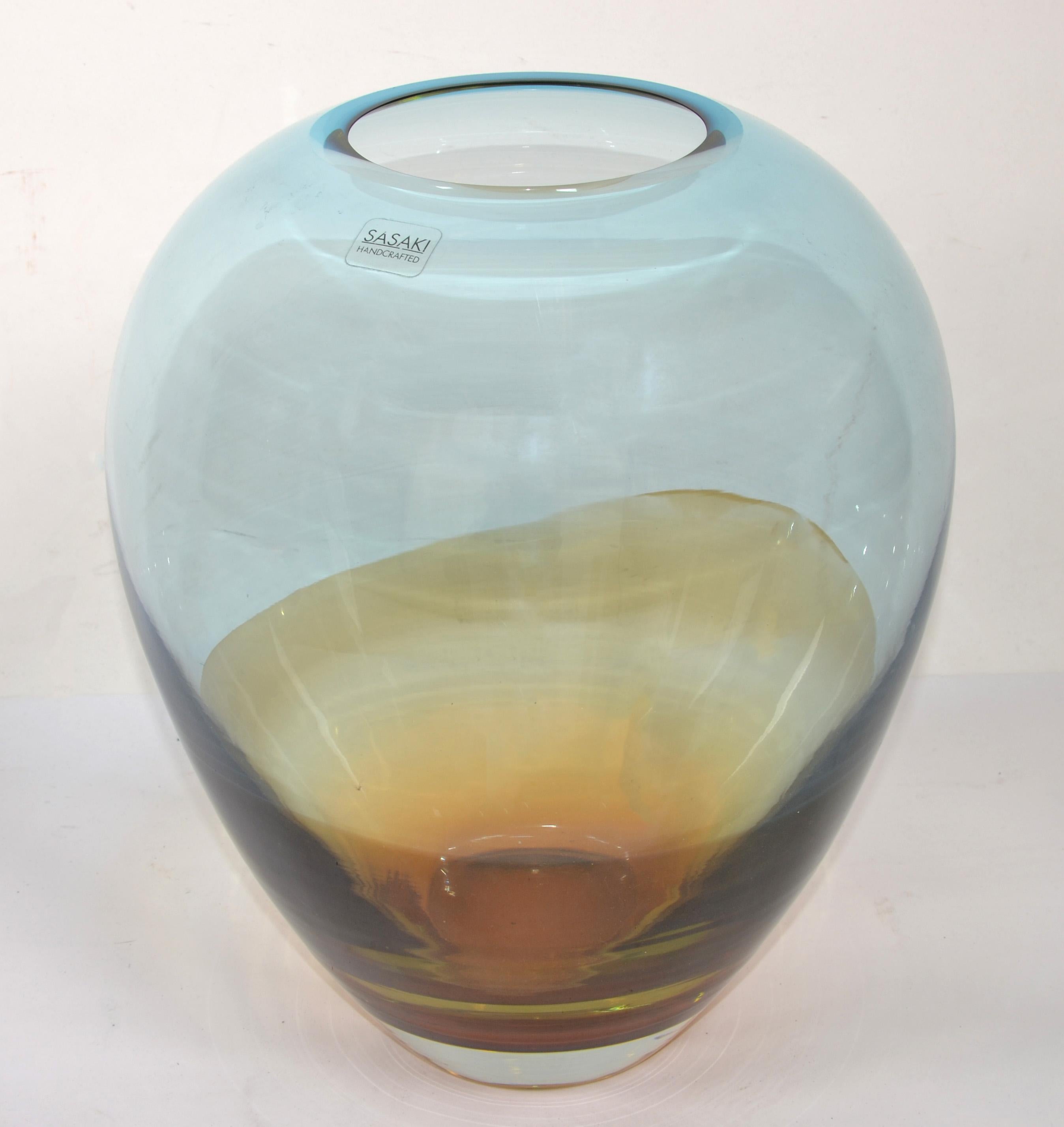 Sasaki Handcrafted oval encased Art Glass flower vase in Baby Blue and hue of Amber Gold with transparent interior.
Venetian Blown Murano Style and a very heavy Vessel, Centerpiece or Flower Vase.
Marked Sasaki Handcrafted at the Top.
In good