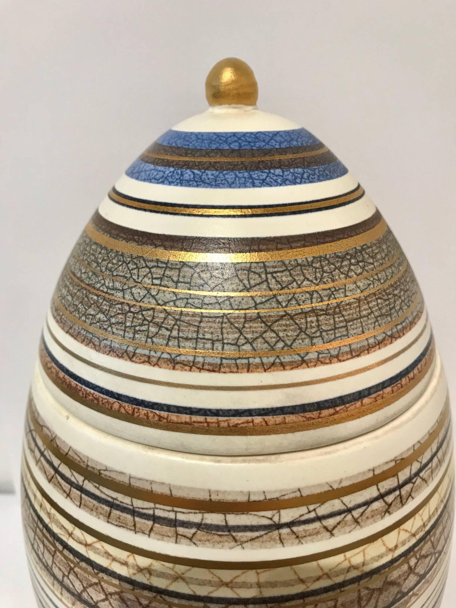 This vintage 1950s Sascha Brastoff egg is a great find for any collectors of midcentury decor. The egg stands on three small feet with a removable lid. It is decorated in distinctive rings of blue and gold with crackle paint.