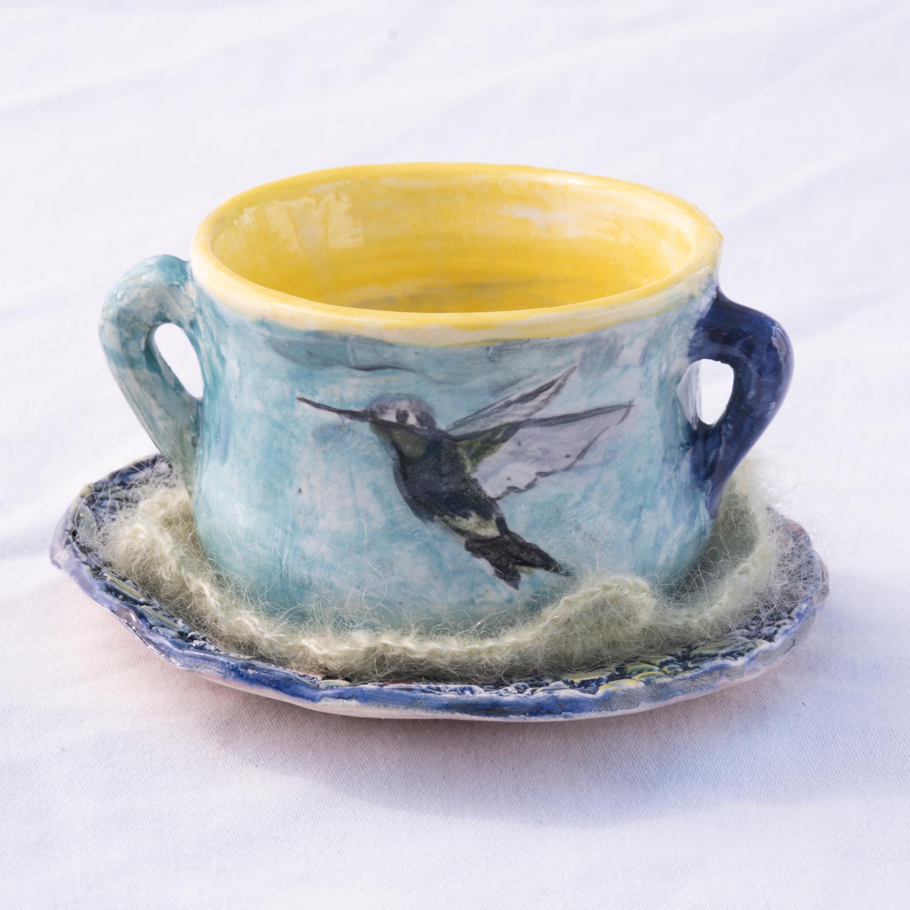 Sascha Mallon’s stoneware tea set, “After the Rain” features a hand-painted underglaze of soaring ravens and swallows on the central teapot.  Each of the accompanying teacups (nestled on cashmere crocheted doilies) depict a different bird: a