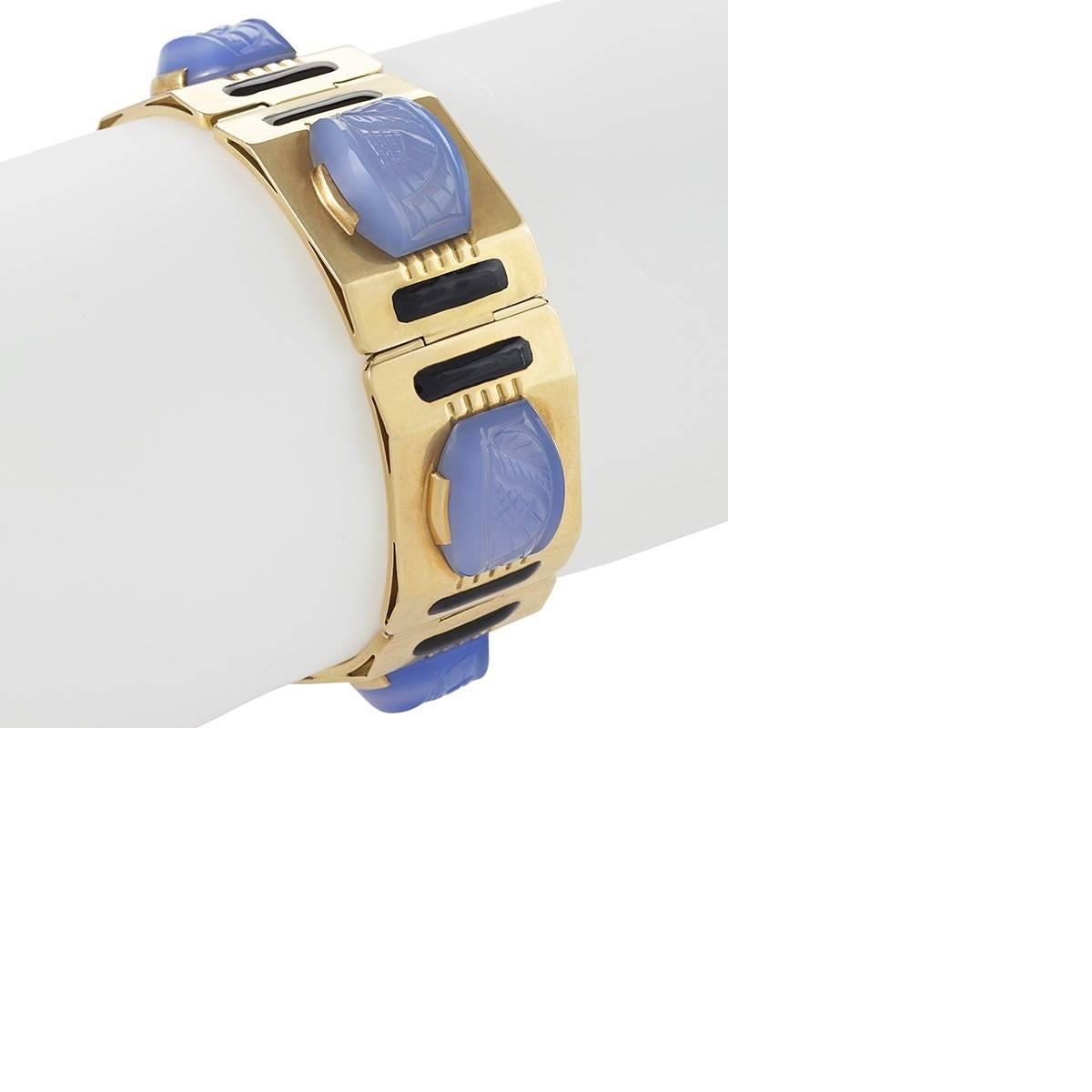 Created in the 1950s, this Sasportas bracelet is composed carved blue chalcedony, polished gold, and black enamel. Designed as a plaque bracelet of canted edges and reverse arches, each link is set with stylized, leaf-carved chalcedony tablet