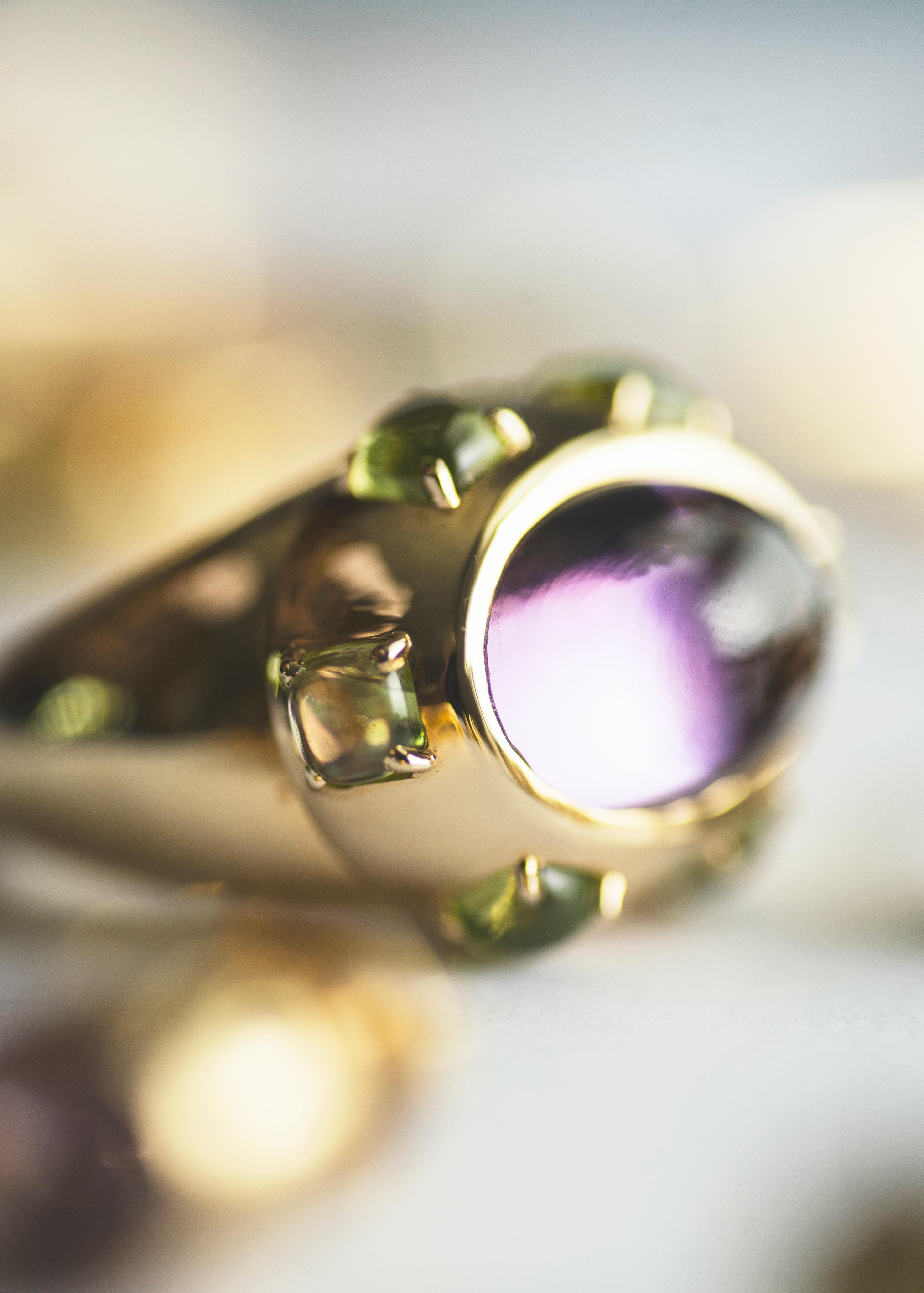 Make a statement with this stunning cocktail ring from Sassi Fine Jewellery's Secret of Berenice collection. Crafted from 18k yellow gold, the ring features a mesmerising Amethyst cabochon of the purest quality, surrounded by six cushion cut