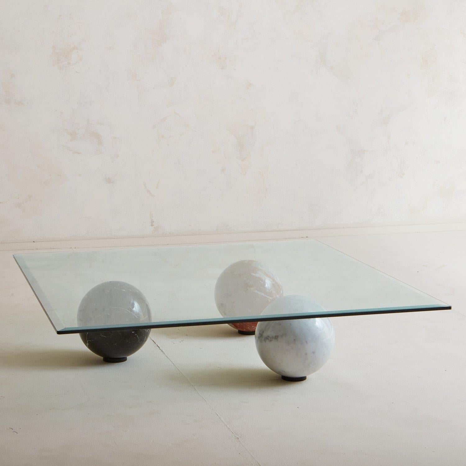 A gorgeous coffee table attributed to Italian manufacturer Cattelan Italia in the 1990s. This table features a marble base formed with three spheres in white, black and red with beautiful veining. It has a square glass tabletop with a beveled edge.