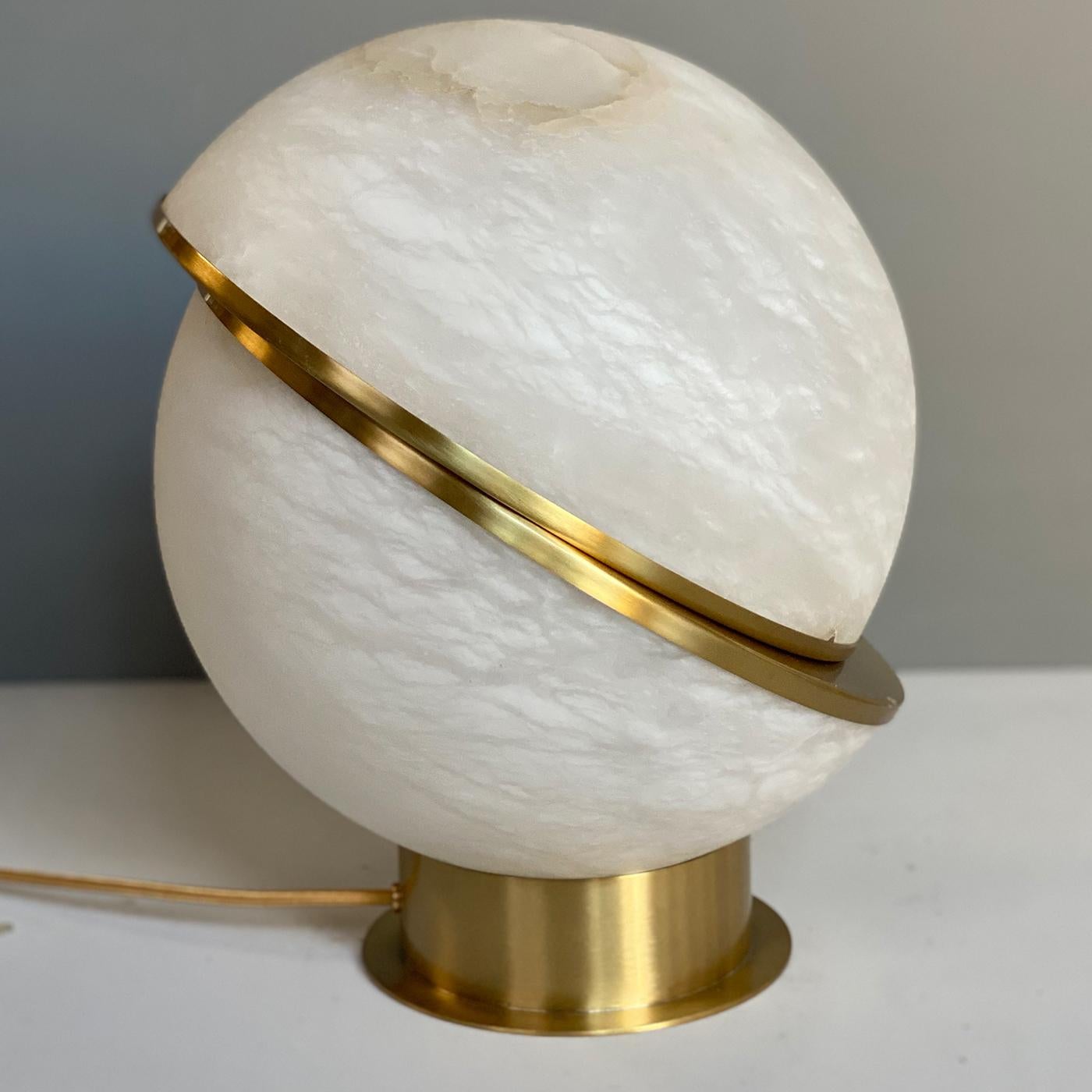 L'Alabaster Globe est une lampe de table composée de deux demi-sphères en albâtre maintenues ensemble par un fin contour en laiton. Combinant l'allure éthérée de la pierre d'albâtre et le reflet chaleureux du laiton, cette lampe est un complément