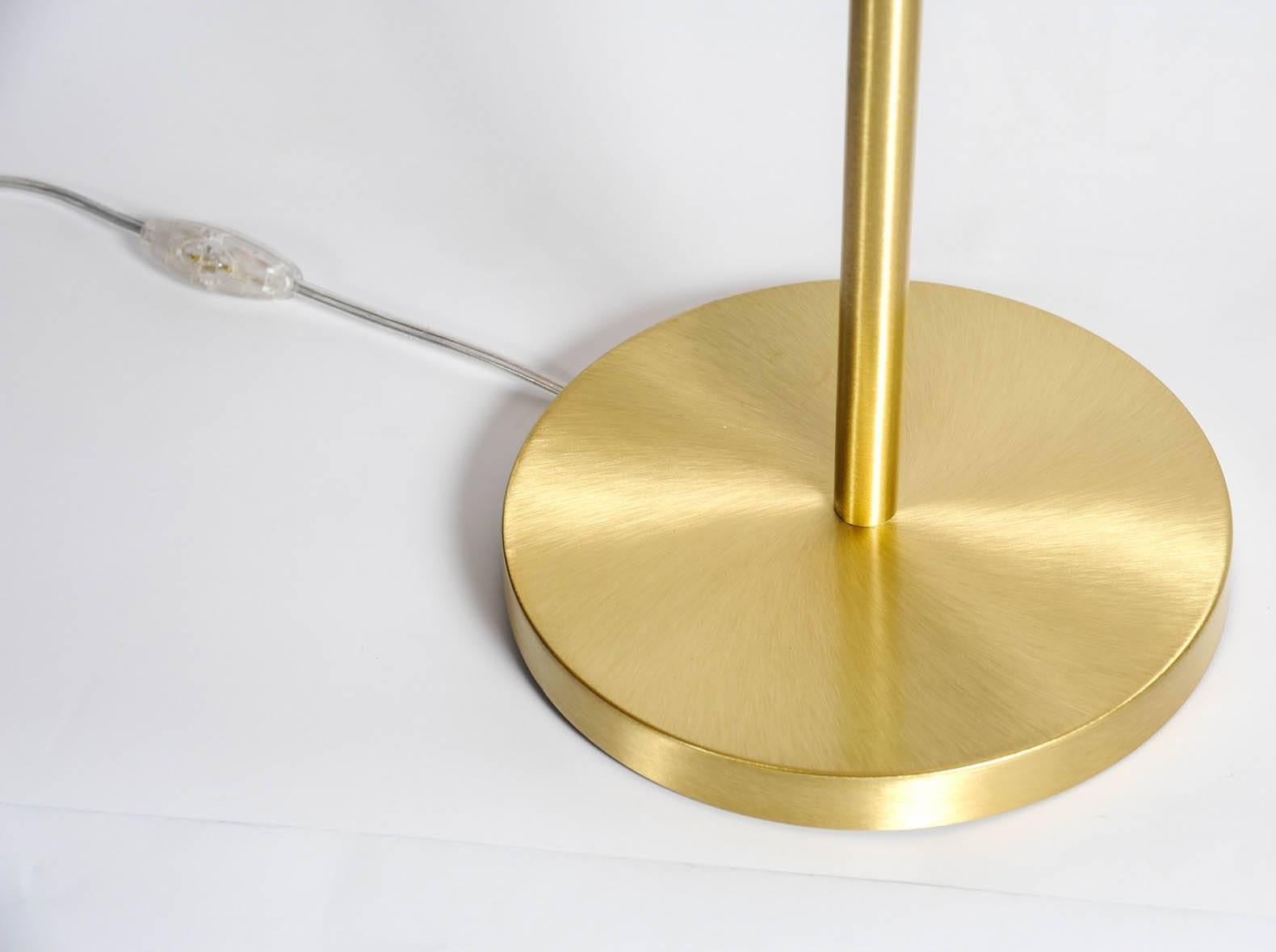 Belles et élégantes lampes de table en laiton satiné à pied rond et tige verticale tenant un globe ovale blanc diffusant la lumière.
