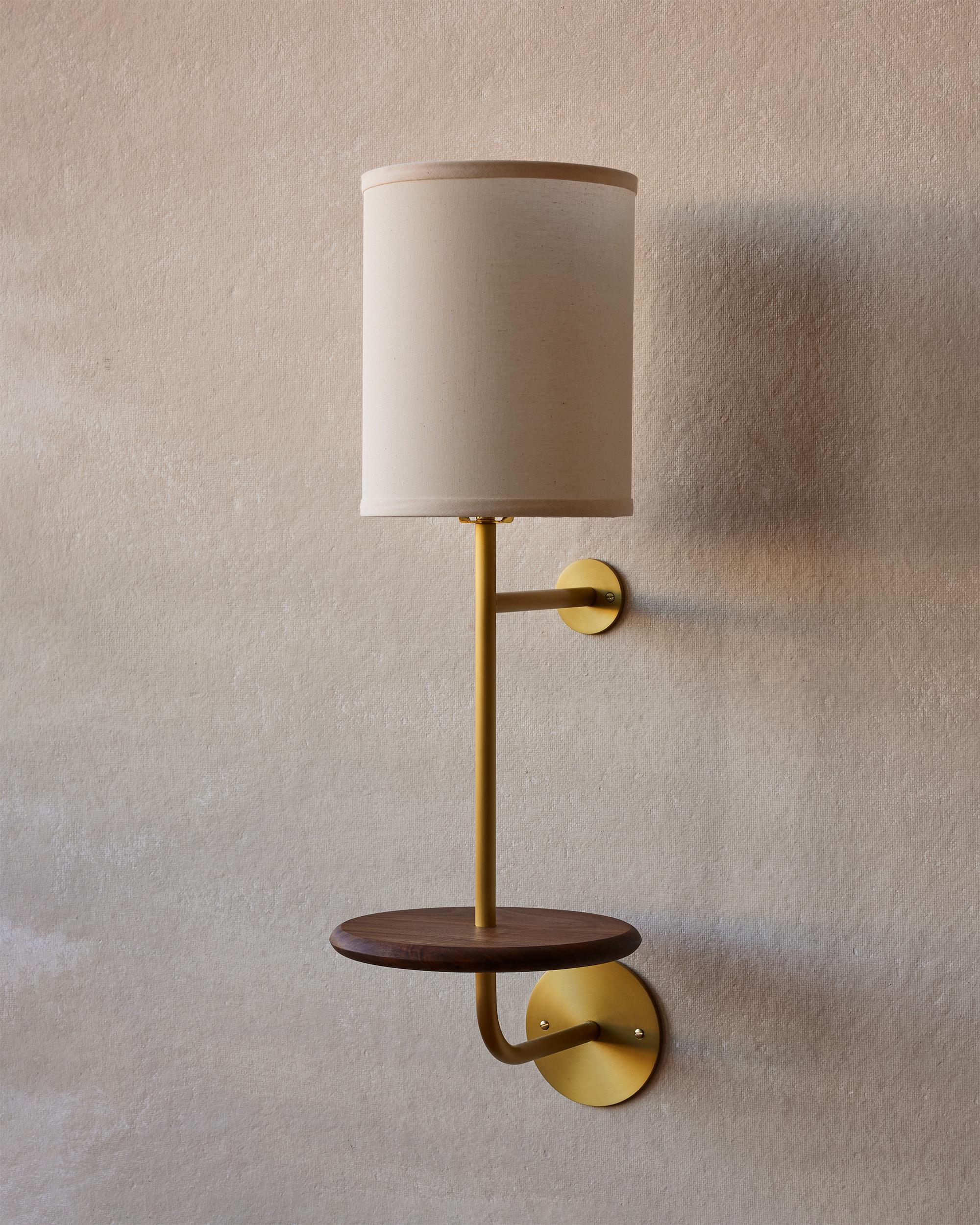 Midcentury inspired satin brass sconce with black walnut shelf. A nod to midcentury lines, the Gustav Sconce is a shining example of balanced design. The rounded satin brass body creates a graceful contour capped with a textured natural Belgian