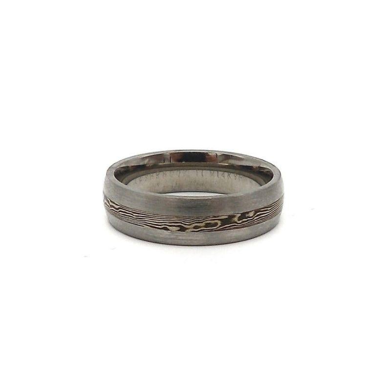 
Dieser schlanke und moderne, satinierte 6 mm breite gewölbte Titanring verfügt über eine wunderschöne 2,5 mm Mokune Gane-Einlage aus 14-karätigem Gold und Kobaltoxid. 