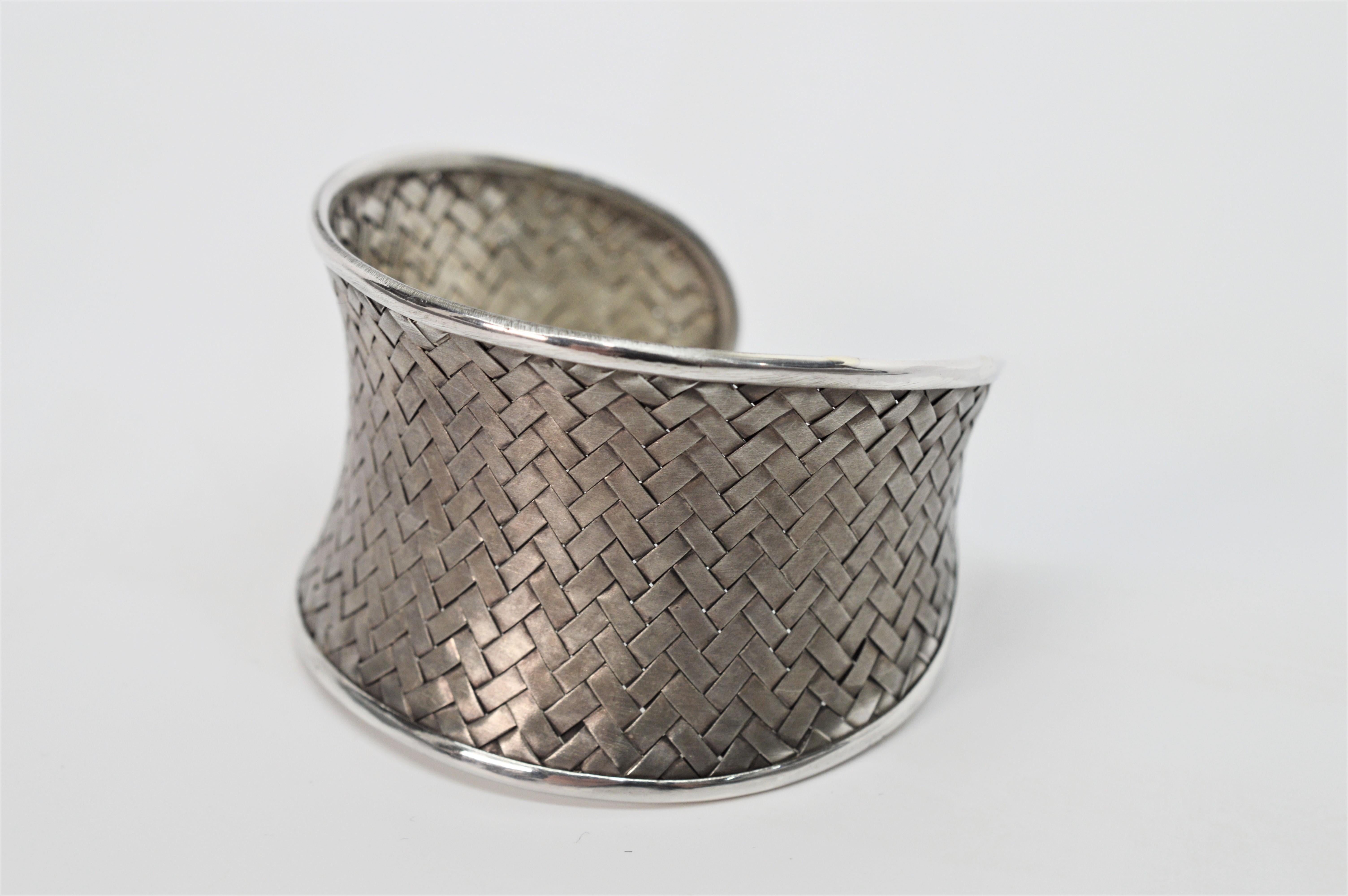 This contemporary silver cuff bracelet displays plenty of texture and flair in its unique basket weave design. Handmade by Mikolay of Chappaqua, the fine silver weave with a pleasing satin patina has a concave shape and is framed with contrasting