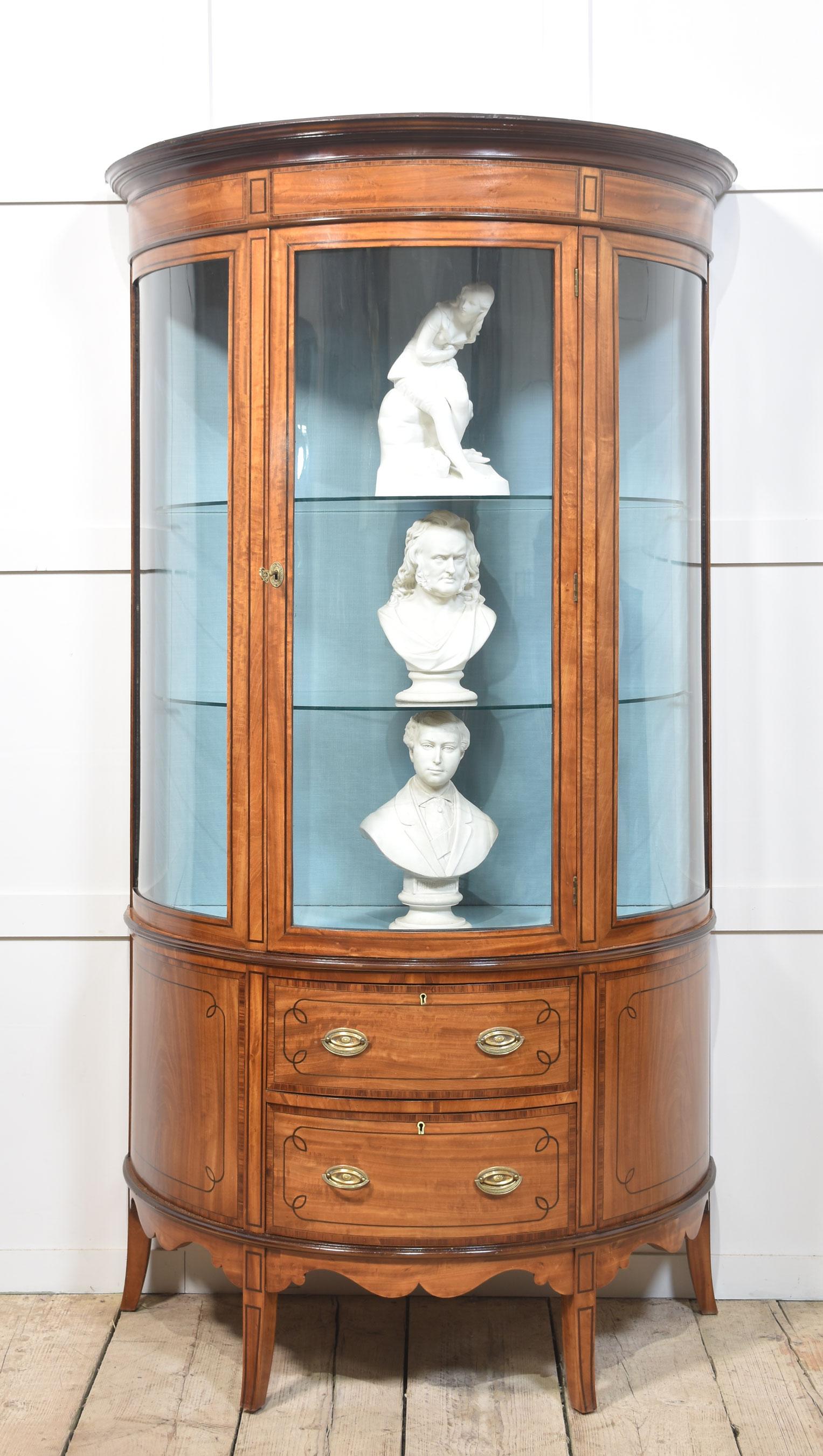 Satinwood display cabinet the moulded top above the large central door opening to reveal watermark silk upholstered interior fitted with two glazed shelves. To the base section fitted with two drawers having brass handles and ebonised stringing. All