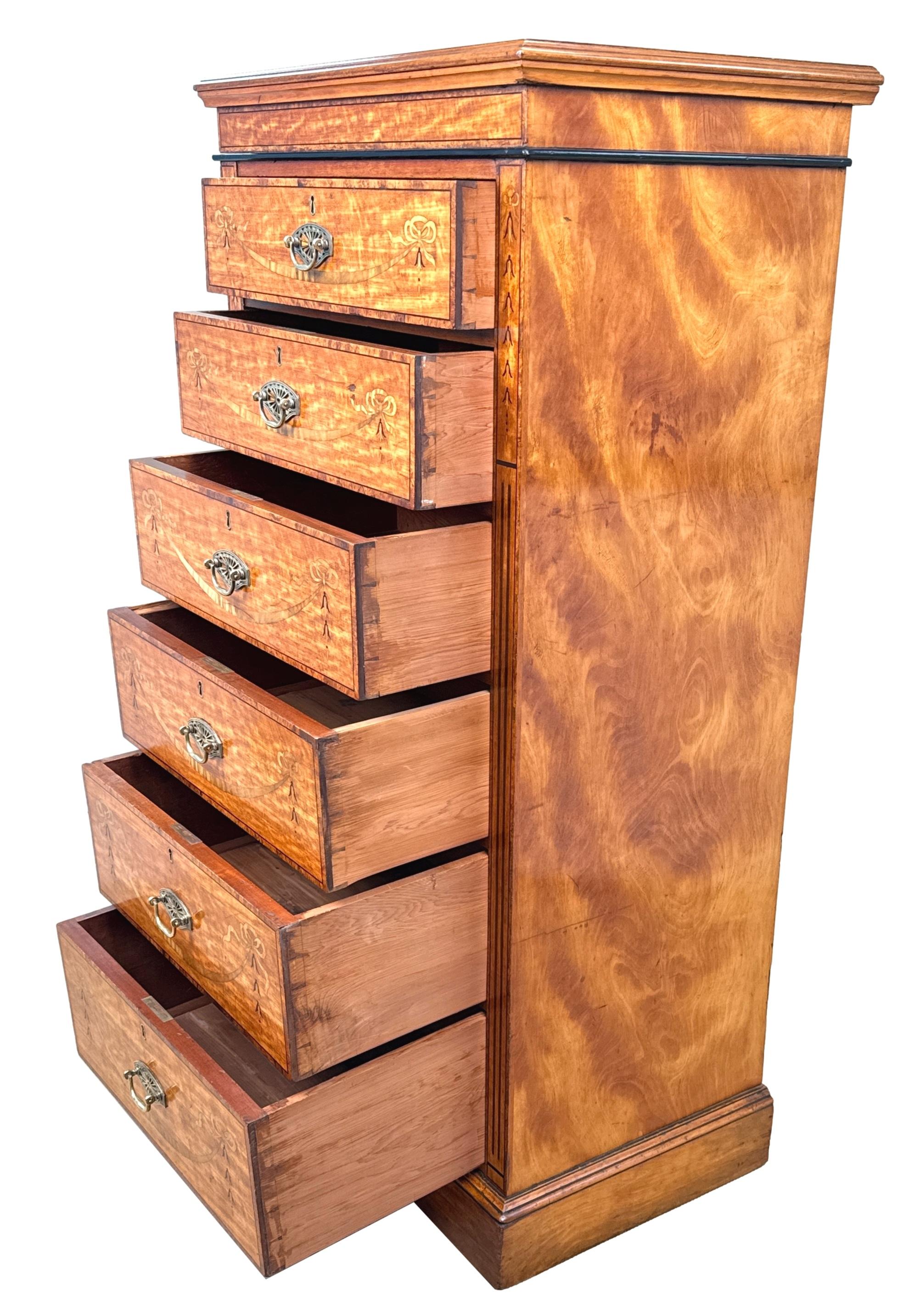 Arcón alto de madera de satén del siglo XIX, de impresionante calidad, con tapa rectangular bien perfilada y seis cajones, con tiradores originales de latón perforado y una excepcional decoración con incrustaciones de cintas, guirnaldas y
