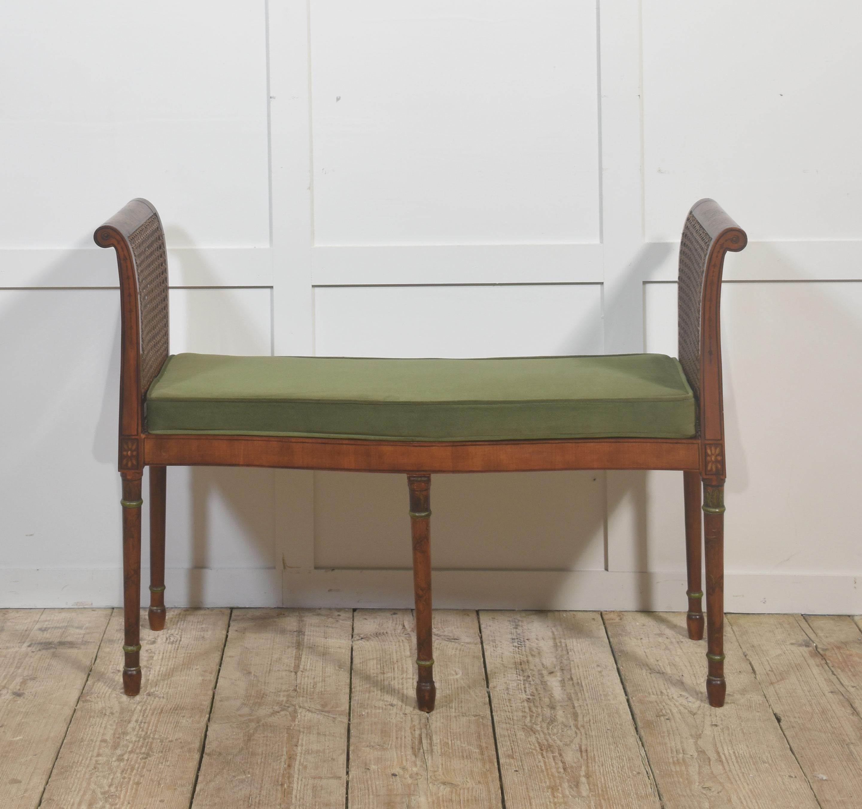 Un banc en bois de satin finement réalisé avec des extrémités à volutes, chacune équipée d'un panneau de canne tressée et décorée de motifs néoclassiques peints à la main comprenant des gerbes de fleurs, des guirlandes nouées par des rubans et un