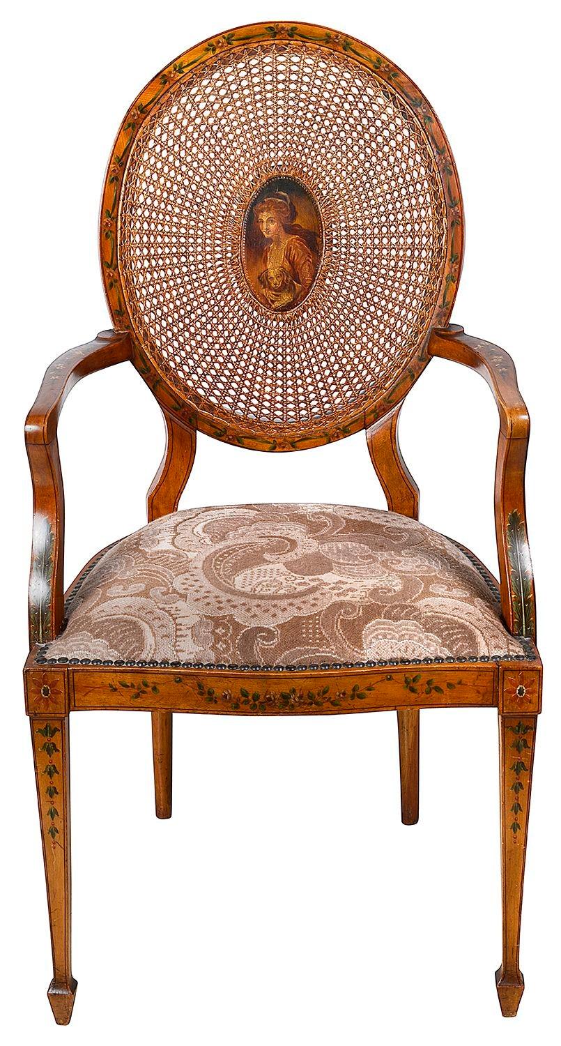 A very good quality Edwardian Satinwood Sheraton revival arm chair, having cane to the oval back rest, hand painted floral decoration to the show wood, a portrait painted to the centre. A stuff over upholstered seat and raised on elegant square