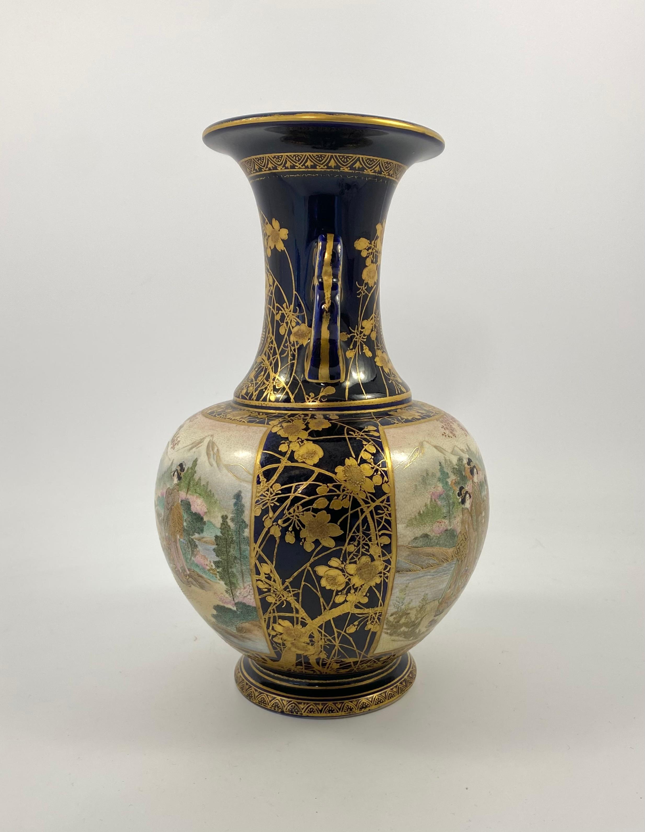 Satsuma earthenware vase, Kinkozan, Meiji Period. The large vase, beautifully hand painted with twin panels of Bijin conversing in garden settings, before a mountainous river landscape. All upon a cobalt blue ground, heavily gilded with a profusion
