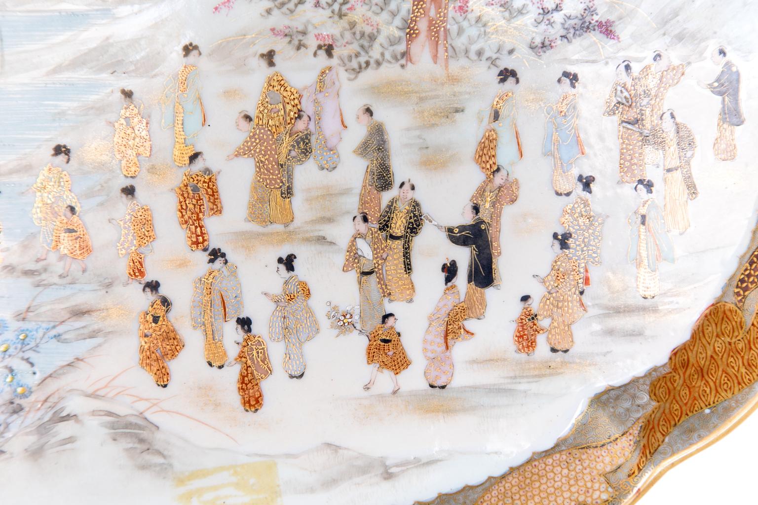 Satsuma porcelain tray, depicting multiple court figures surrounding and wading in a lake. The figures are adorned with abundant and finely detailed gold with landscape in the background. The angled gallery is decorated with intricately painted gold