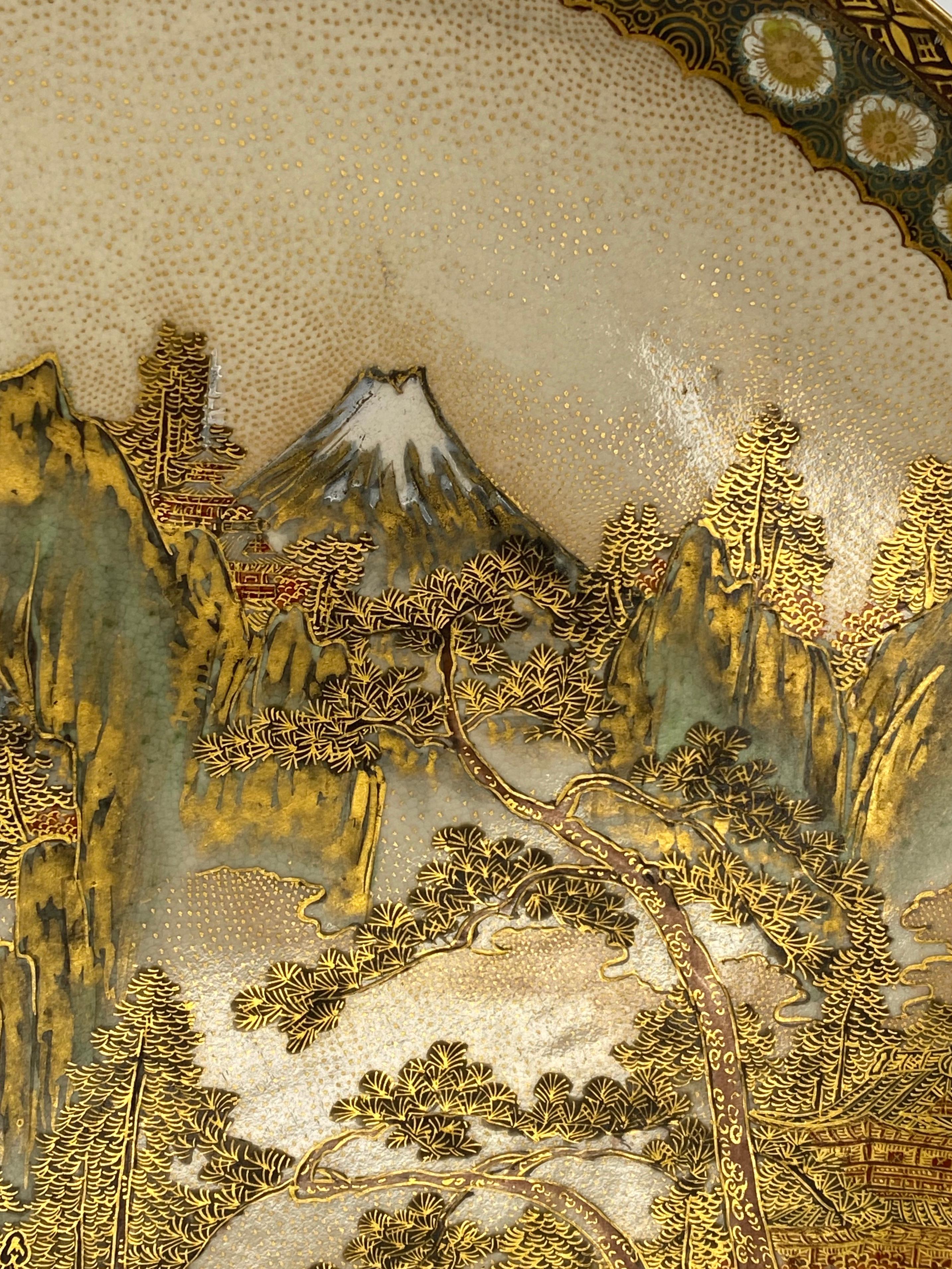 Satsuma pottery plate, Kinkozan, Japan, circa 1900. Meiji period. The plate well painted and gilded, with figures on a promontory, looking towards temples, beneath Mount Fuji. All within an elaborate textile motif border.
Signed to the reverse