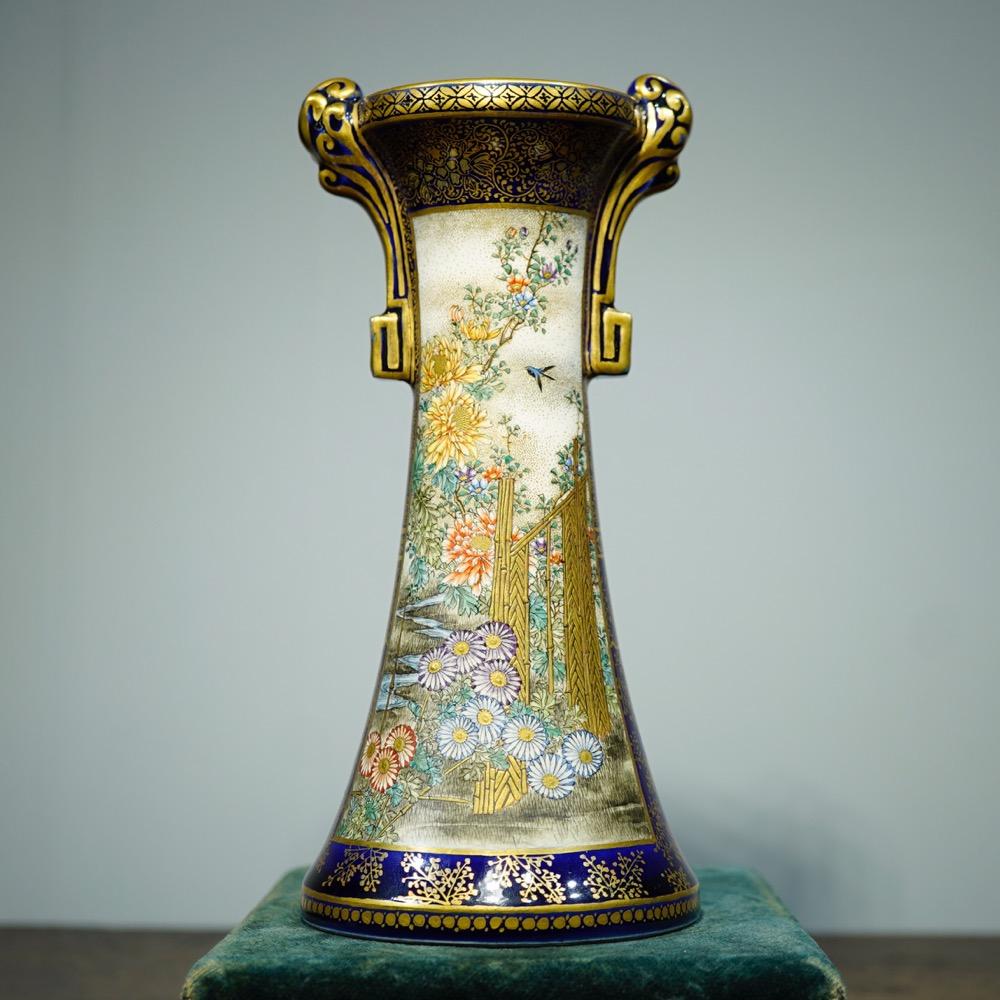 Satsuma vase of tall form with flared base, the lip with two scroll handles supported on square brackets, superbly painted in the studio of Kinkozan with two scenic panels, one of a garden with bamboo fence and swallow, the other with 'every-day