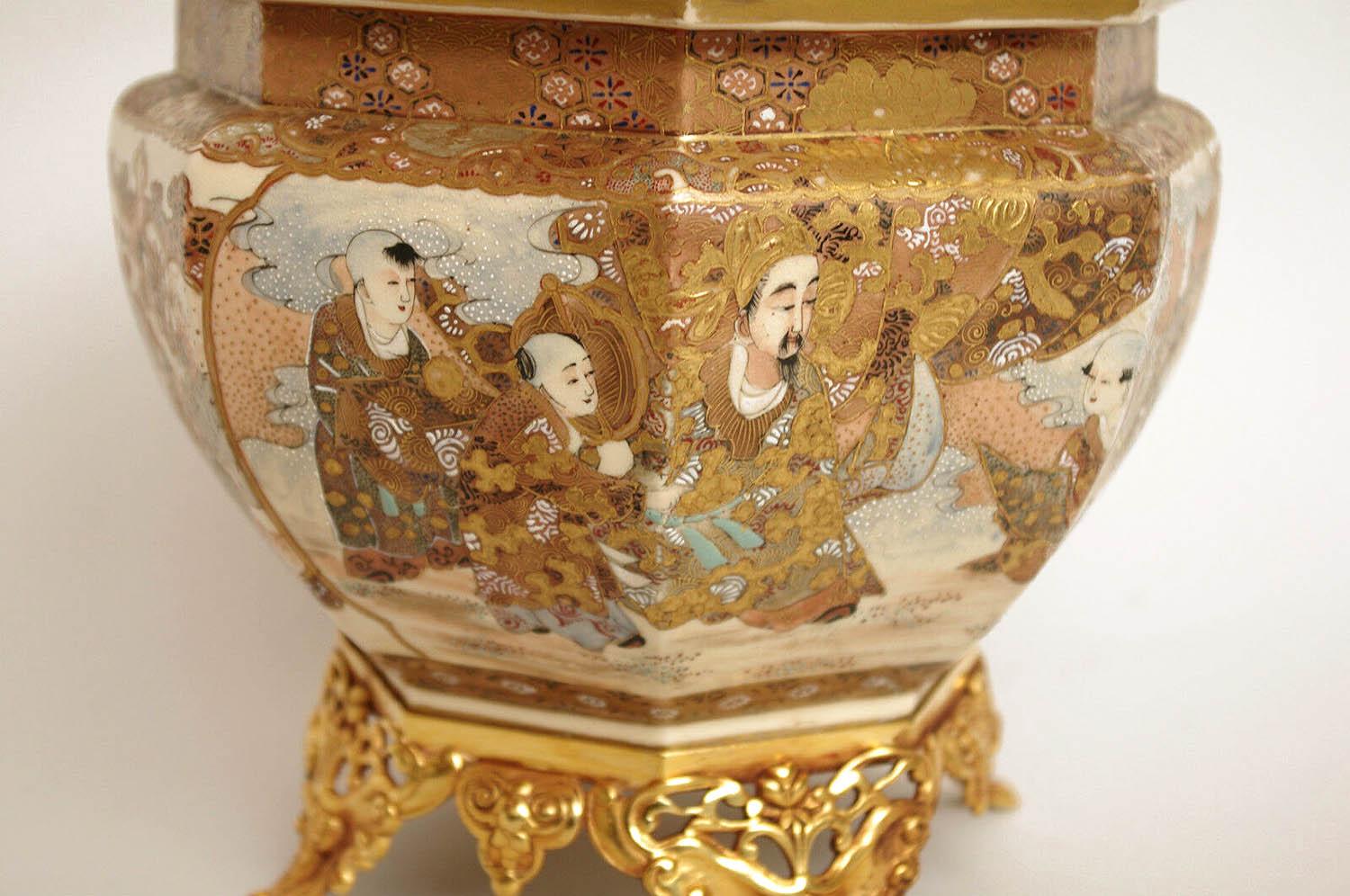 Satsuma ware planter in octagonal jar shape. Decor of polychrome enamels on a white background and gilt highlights figuring two palace scenes in cartouches, surrounded by blue, red and white chrysanthemum. High and low friezes with a geometrical