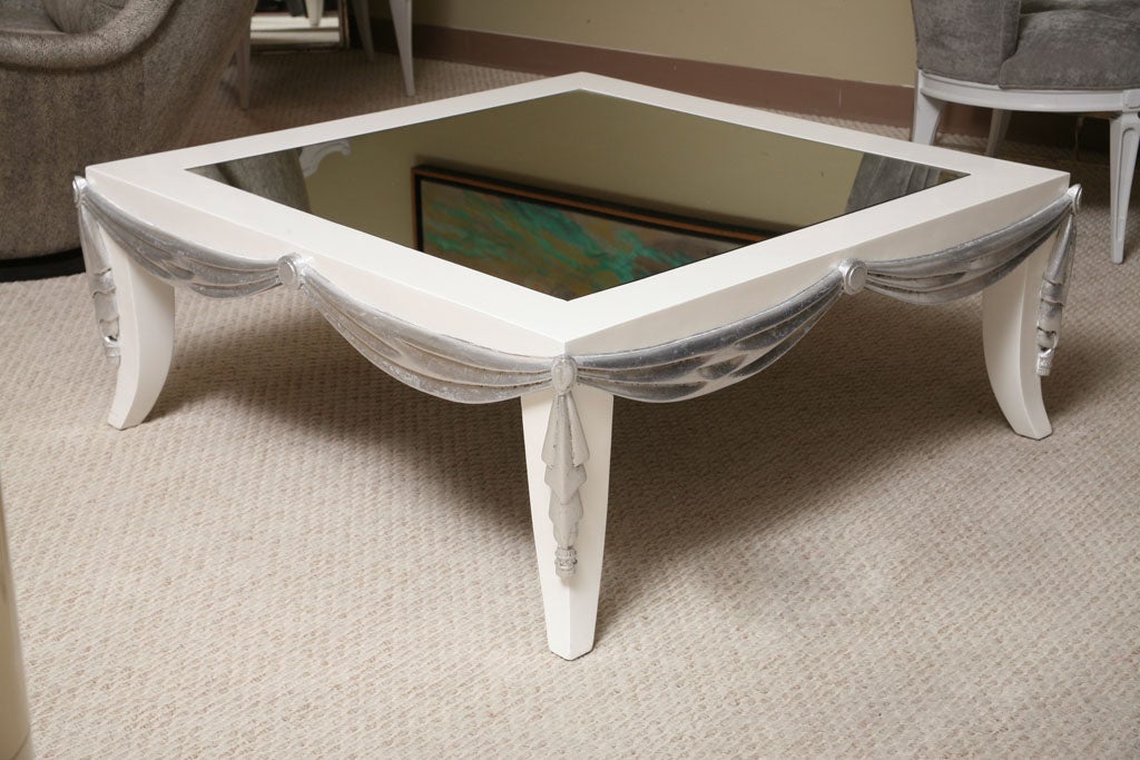 Very unusual coffee table. Wood frame in white lacquer with sculpted draping in silver leaf. The top has a mirror inset.