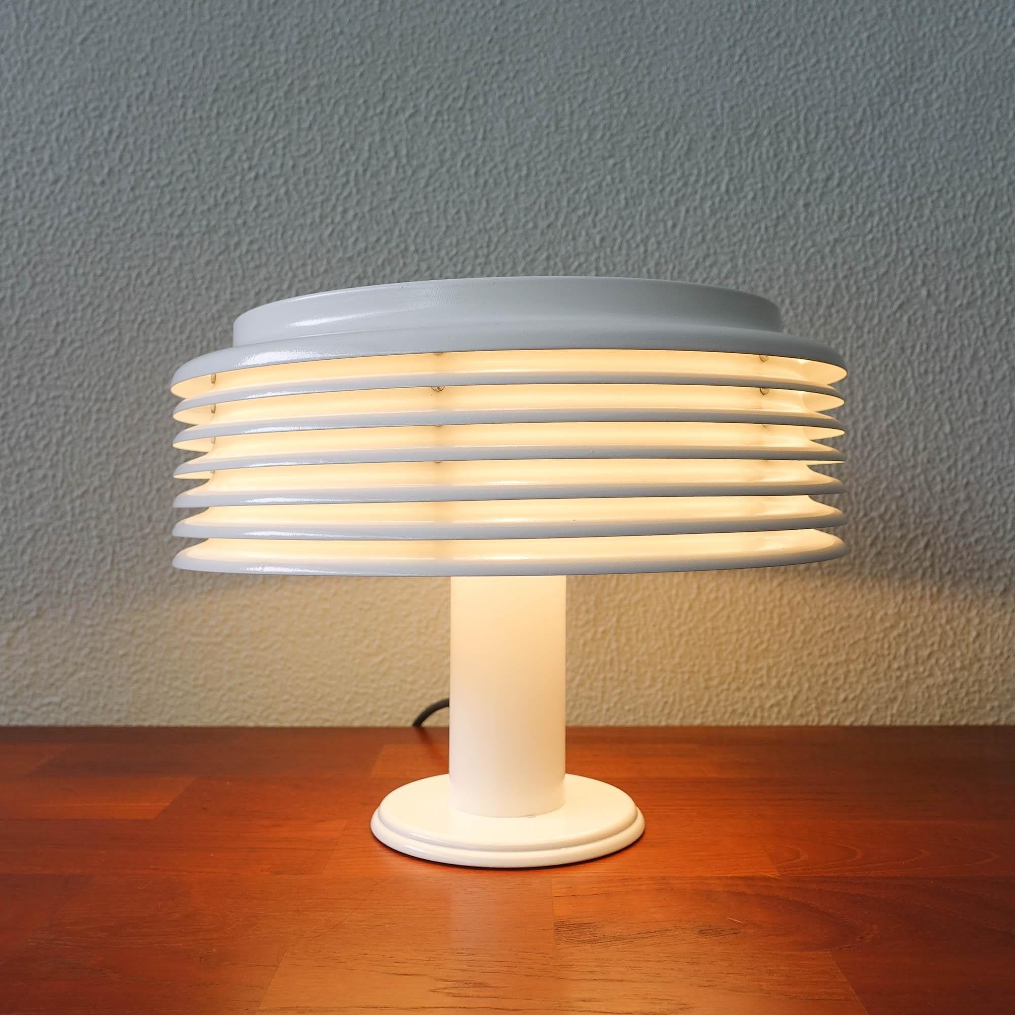 This table lamp was designed by Kazuo Motozawa for Staff, in Germany, during the 1970's. It features a white painted metal round base and tube. White mushroom lampshade made of slat rings. Round metal lid on top. When it's on , it emits an indirect