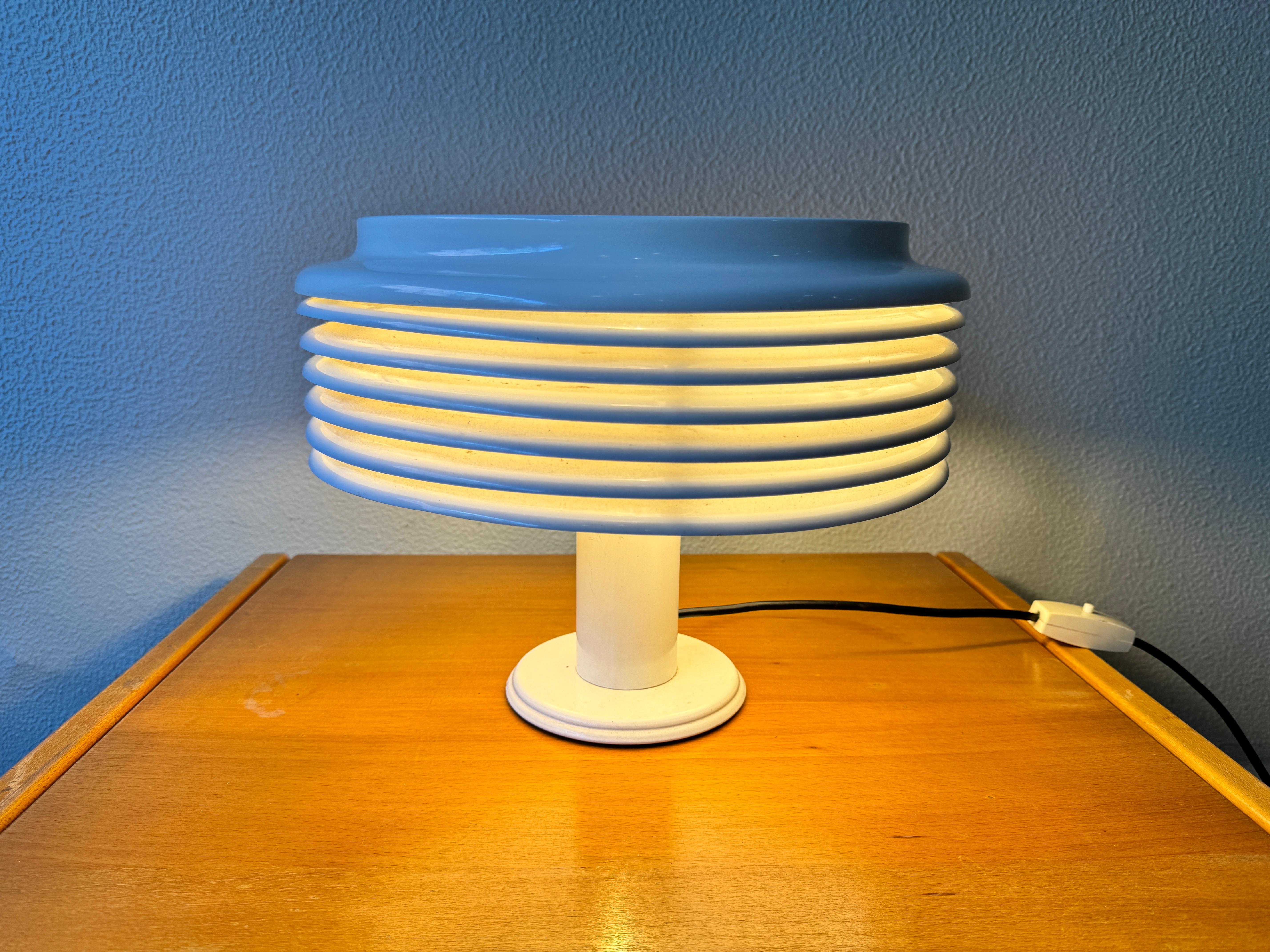 The Saturno Table Lamp by Kazuo Motozawa for Staff Leuchten is a stunning vintage piece from the 1970s. The lamp features a sleek white painted metal base and tube, topped with a unique mushroom-shaped lampshade made of slat rings. The lamp emits an