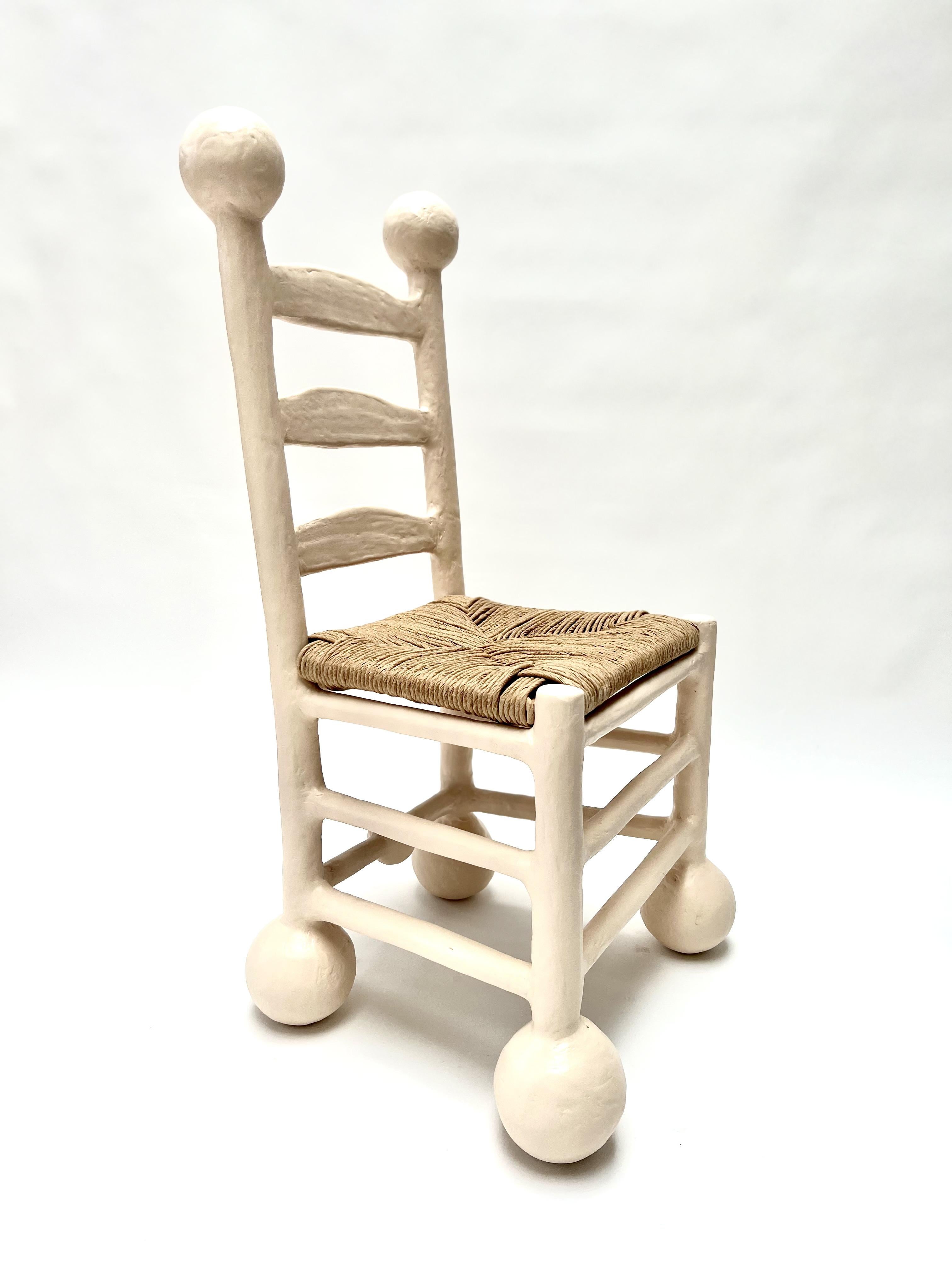 The Saucer Dining Chair by Brent Warr balances playful form with sculptural elegance. Its legs echo the signature stacked-ball motif, grounding the chair with a bold yet refined silhouette. The seat rests within a softened, curved frame, creating