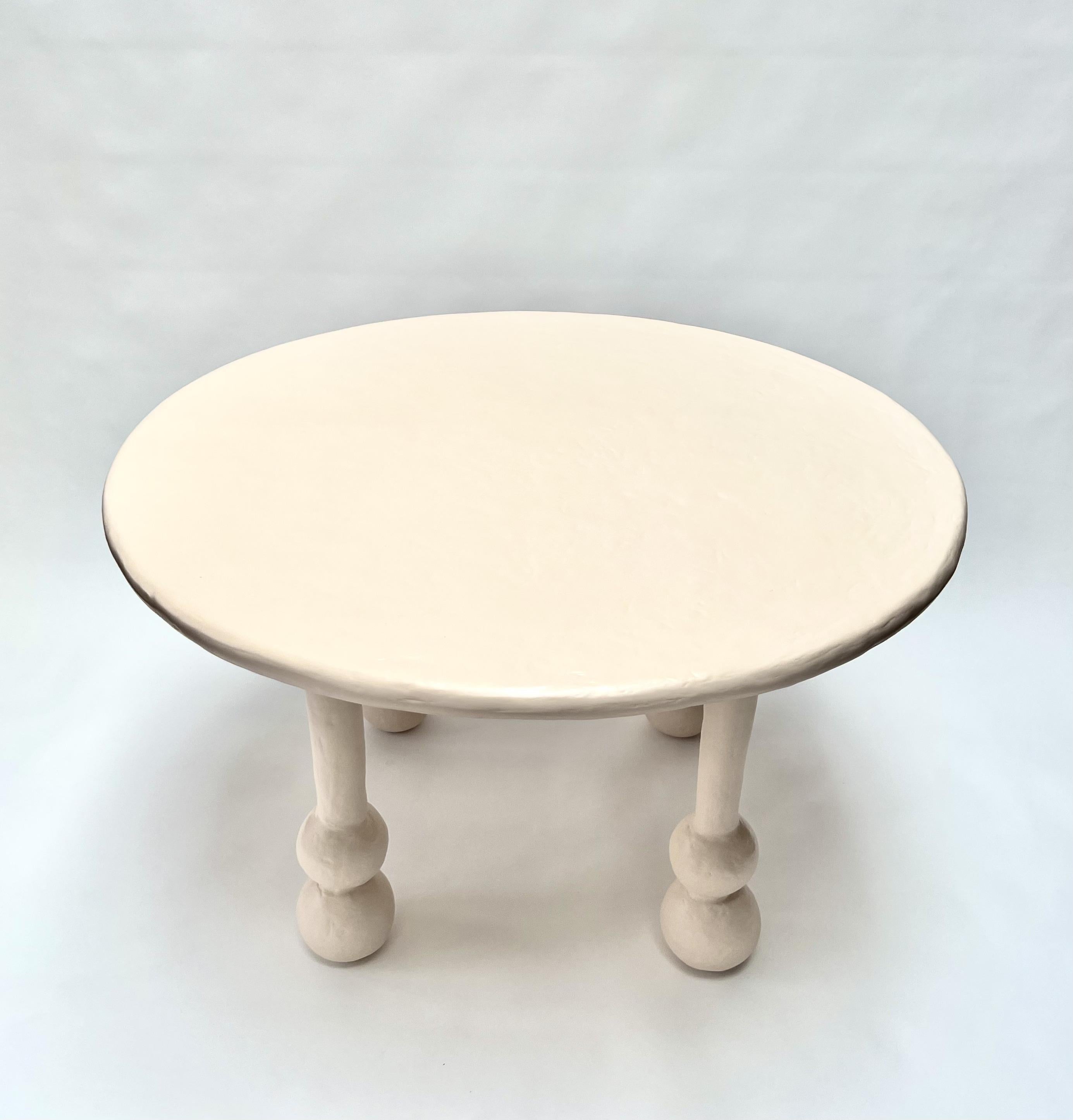 The Saucer Dining Table by Brent Warr features a striking interplay of form and balance. Each of its four legs is grounded by a pair of stacked spherical shapes, creating a bold yet minimal sculptural silhouette. Crafted from a custom gypsum and