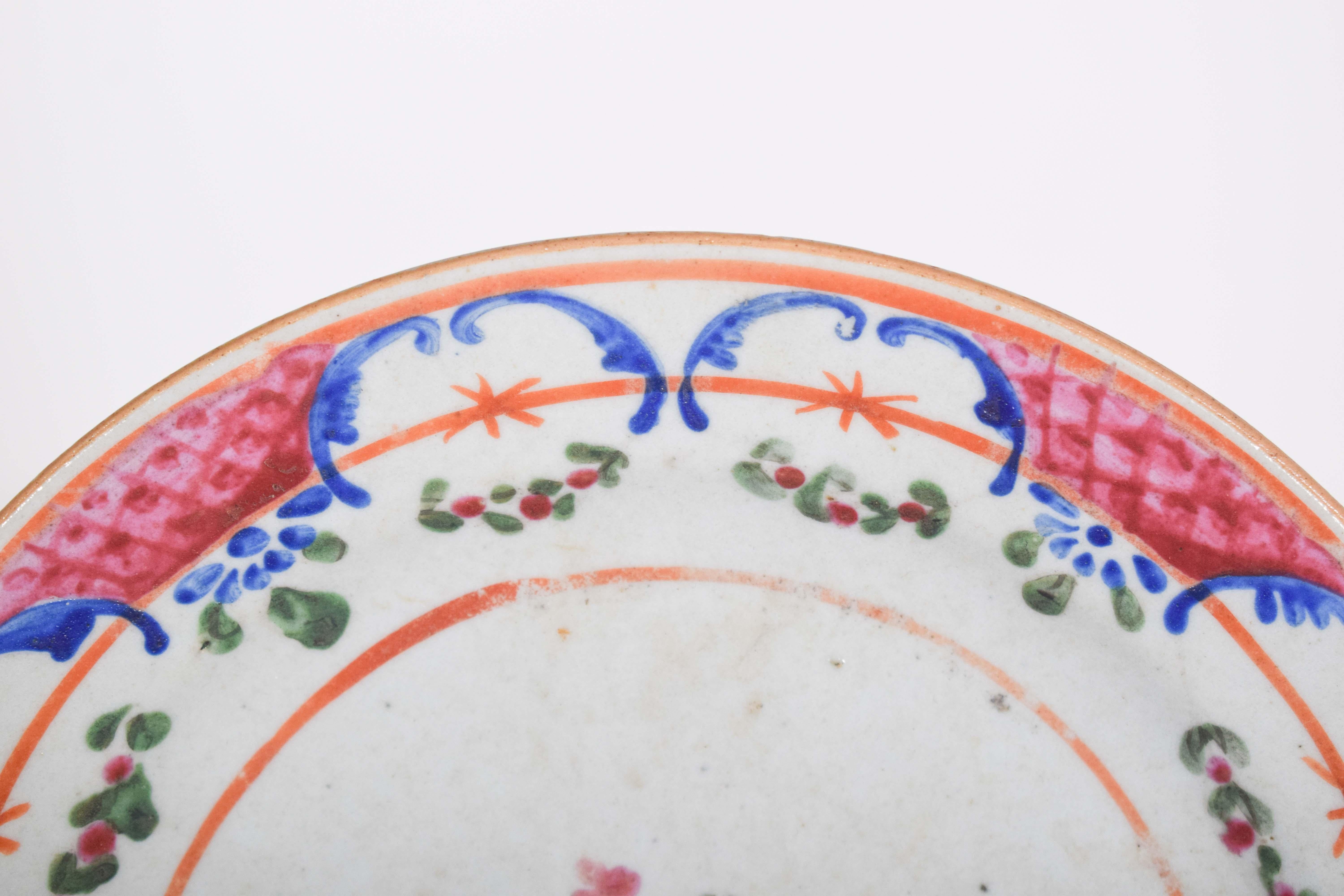 A saucer, made of Chinese porcelain for export, which displays a delicate and elegant decoration, possibly of European origin. It features a refined floral pattern, hand-painted in vibrant shades of pink, blue, green and red, with ornamental details