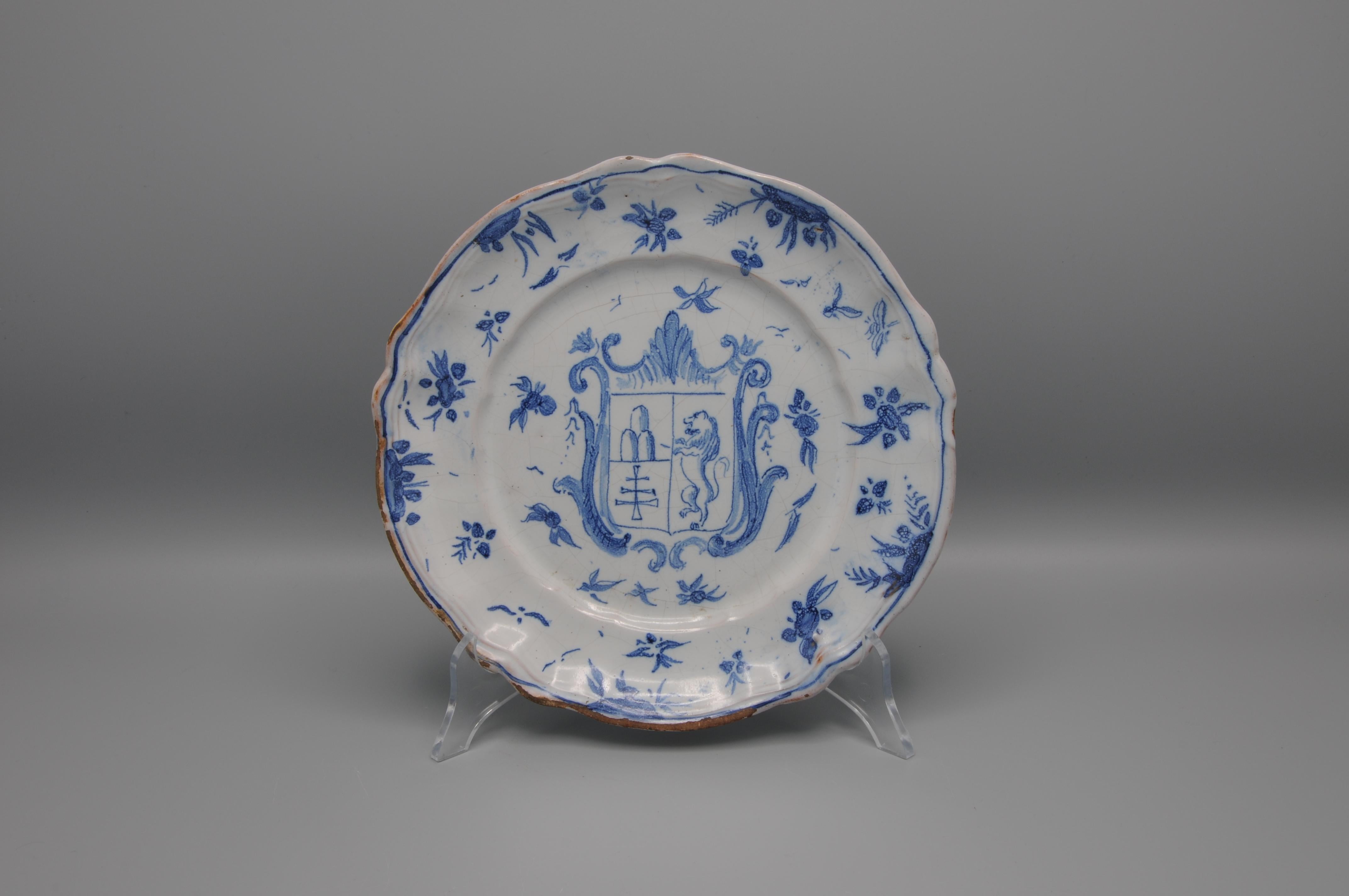 A Savona plate with blue decor. On the front a heraldic coat of arms - divided into two, on the right three mountains and a pontifical cross, on the left a climbing lion- within border with motifs “orientalizzante o a tappezzeria”.

 