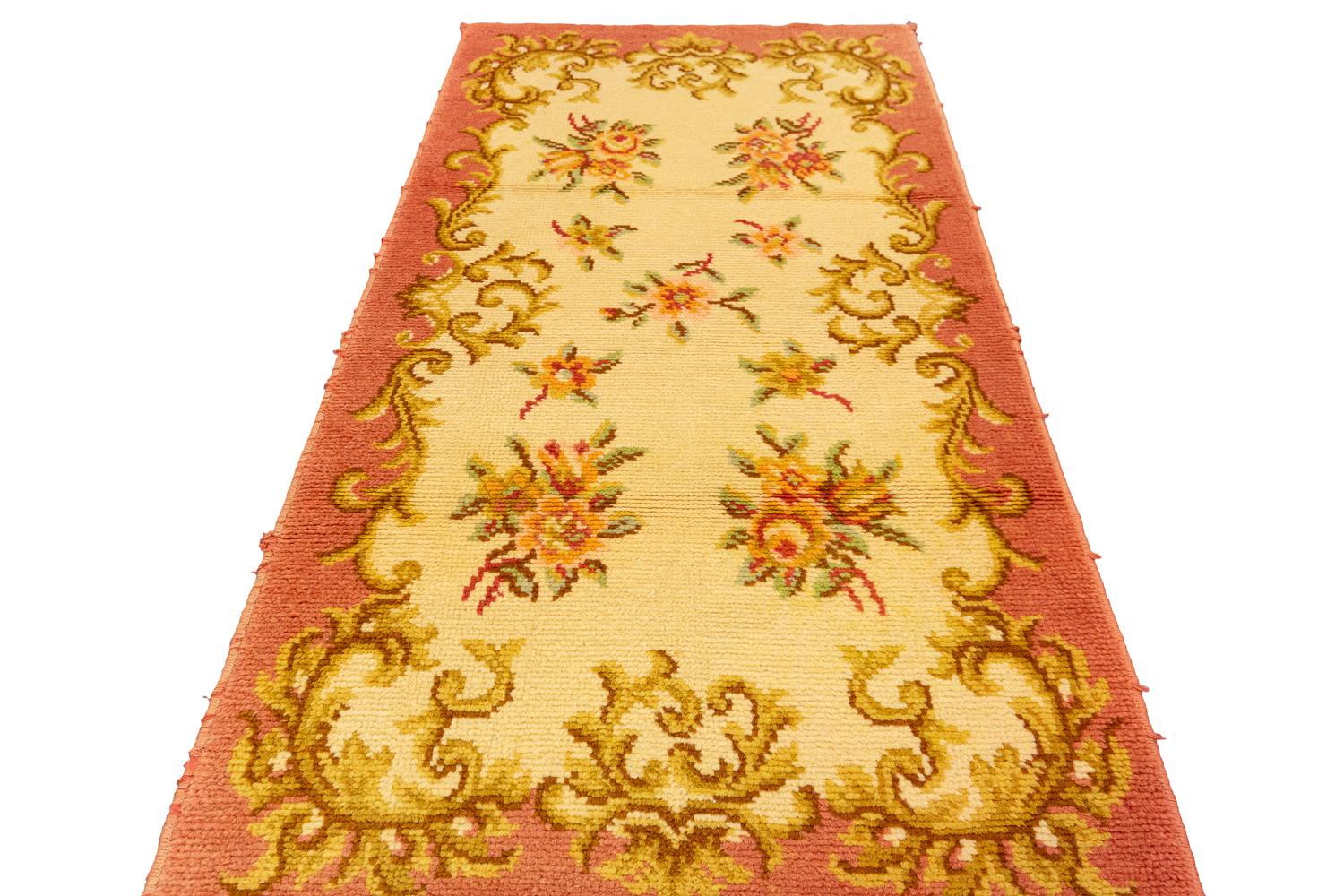 This is a vintage European rug woven during the mid-20th century circa 1950 and measures 141 x 72CM in size. It has a highly classical European drawing with golden-colored curling leaves which create a border and in close a highly spacious all-over