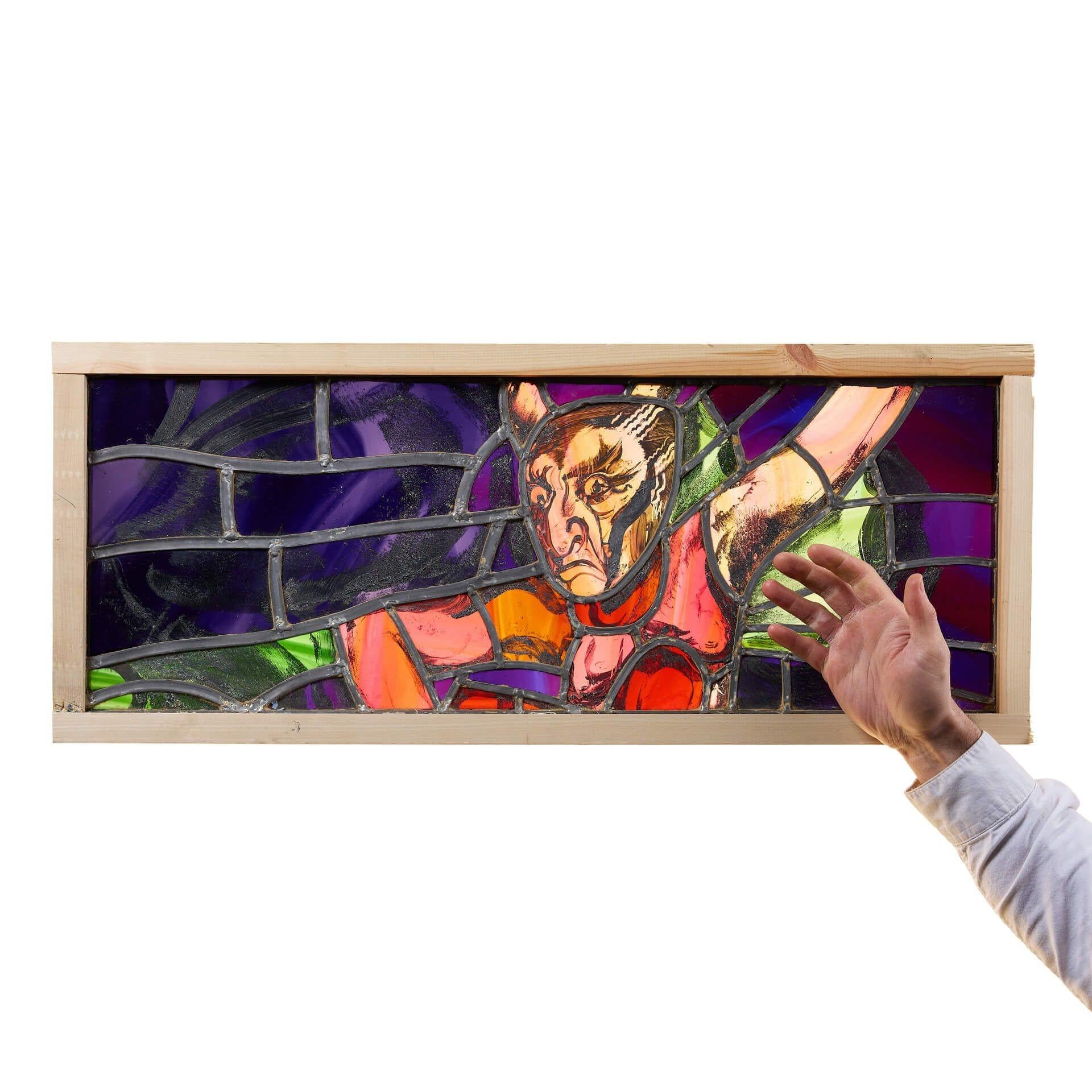 A theatrical stained glass window depicting a winged mythical figure, from the workshops of British stained-glass artist, Sax Shaw.

Beautifully made using glass in shades of purple, red, blue and green, this contemporary stained glass window panel