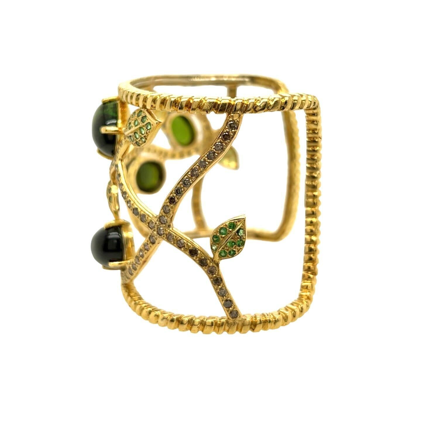 An 18 karat yellow gold, green tourmaline, tsavorite garnet and fancy light brown diamond bracelet, Sazingg.  The wide cuff, with ropework borders, displaying a vine set with four  oval cabochon green tourmalines, the leaves set with approximately
