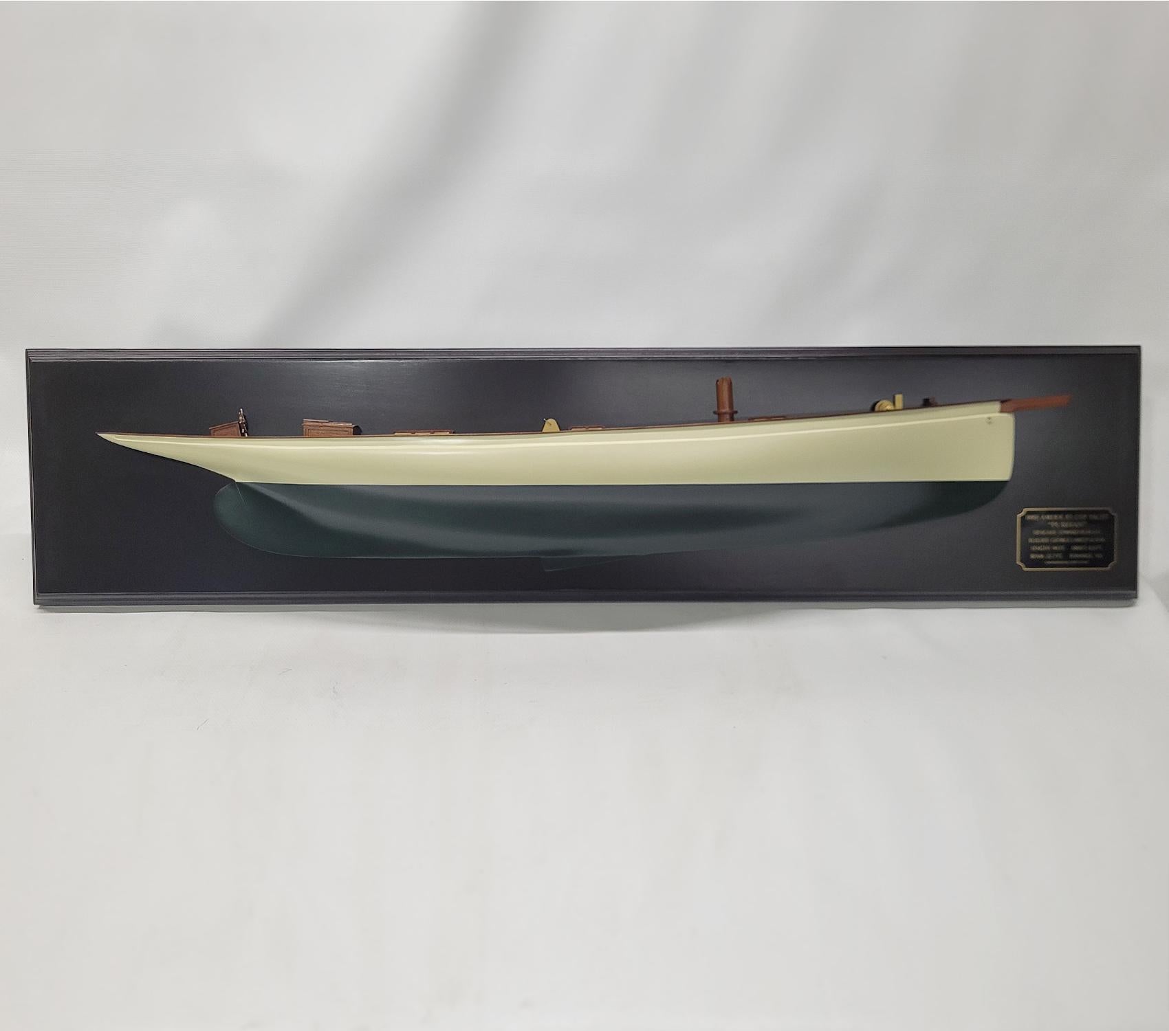 Carved woo half model of the 1885 America's Cup Yacht Puritan. The hull is painted white above the waterline and green below. There is a planked wood. mahogany deck, hatched, skylights, wheel box, companionway, etc.. The hull is mounted to a