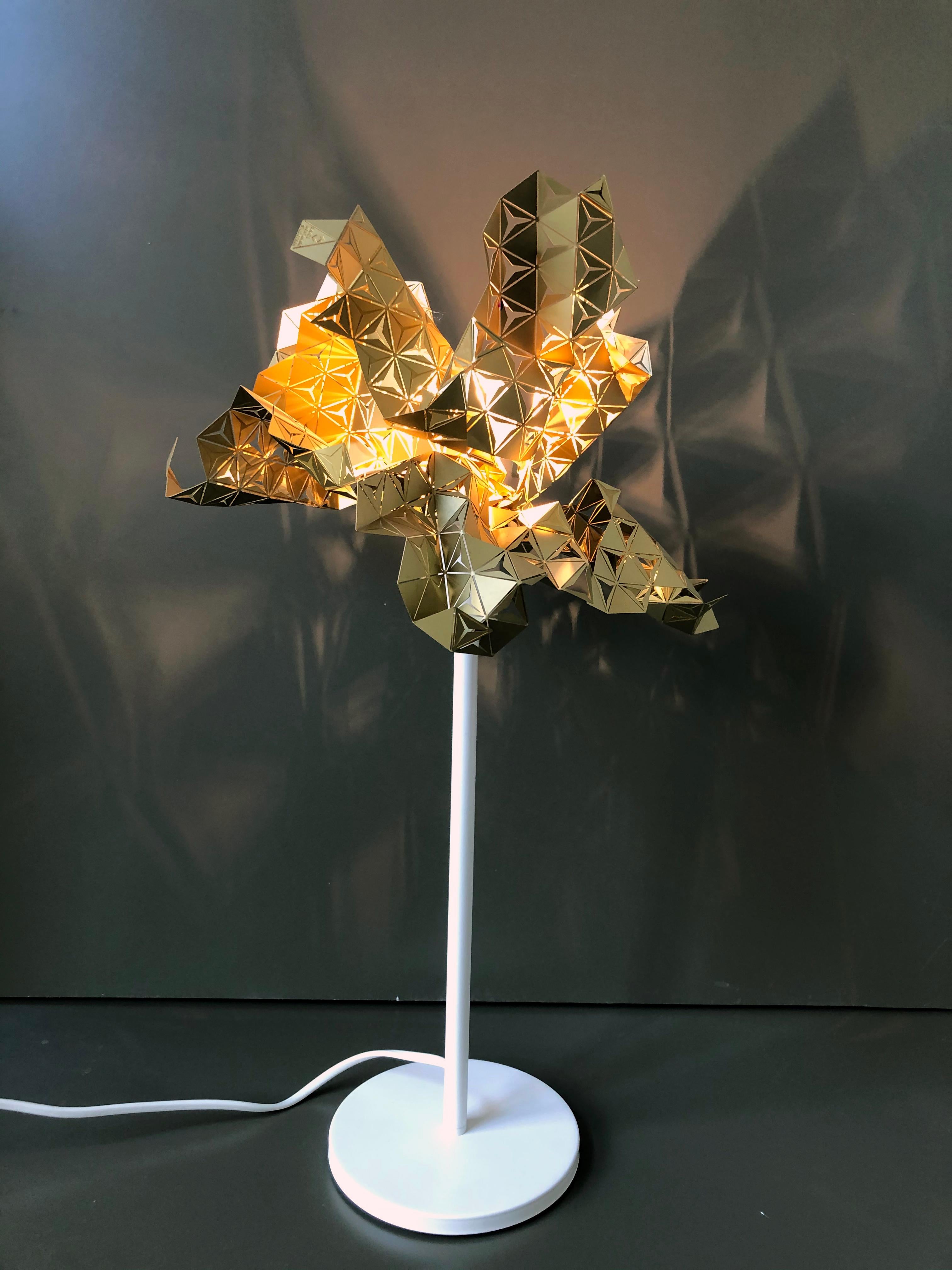 Table lamp  of the Scales collection Satin brass lampshade, white painted metal base.
The lampshade is made of a very thin brass foil with geometric designs. All lampshades are made with the most precise cutting technology, yet the final folding is
