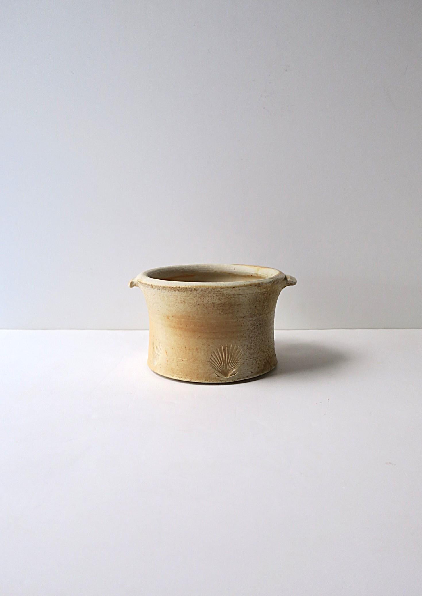 A matte ceramic ice bucket (or bowl pot) with scallop seashell design around. Piece is varying hues of beige/sand with a matte exterior - a slight sand-like feel resembling 'sand' or a 'beach', decorated with embossed scallop seashell design around
