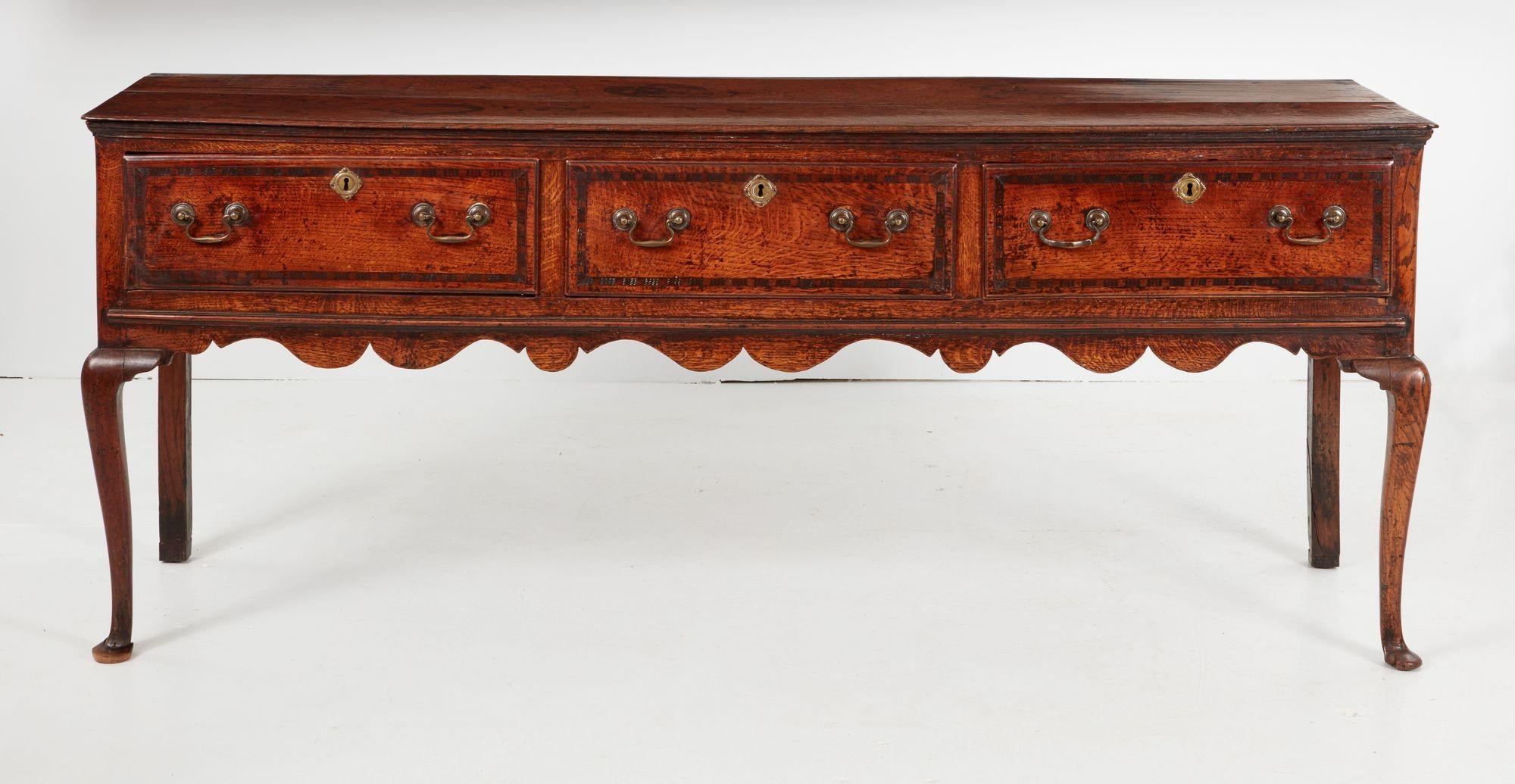 An elegant Welsh oak sideboard or dresser base having two-plank top over three cross-banded drawers above scalloped wave form apron on jaunty cabriole front legs ending in pad feet with straight square section back legs. Molded paneled sides. Good