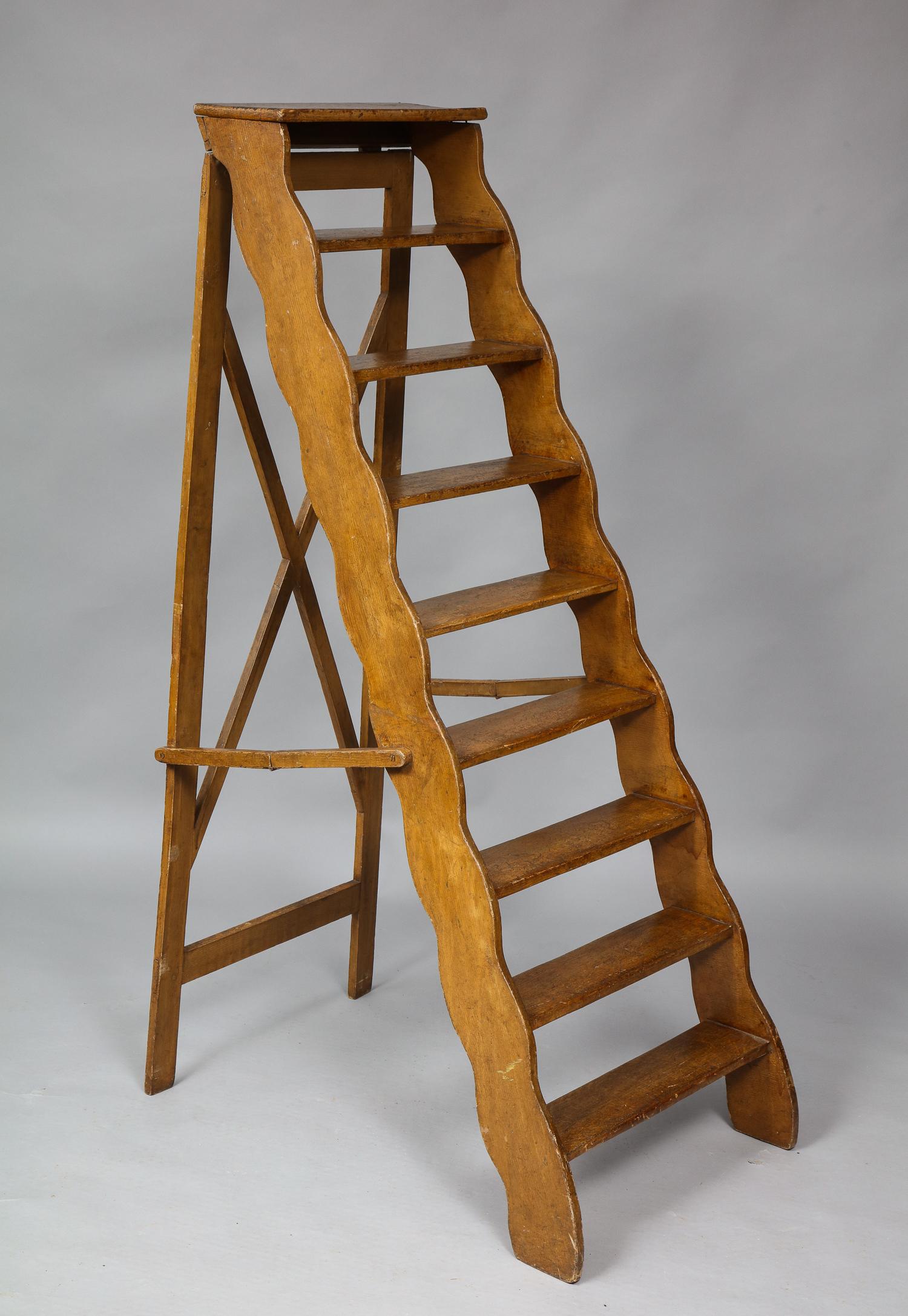 A sculptural and useful 19th century English library ladder having original mustard painted decoration with scalloped sides.