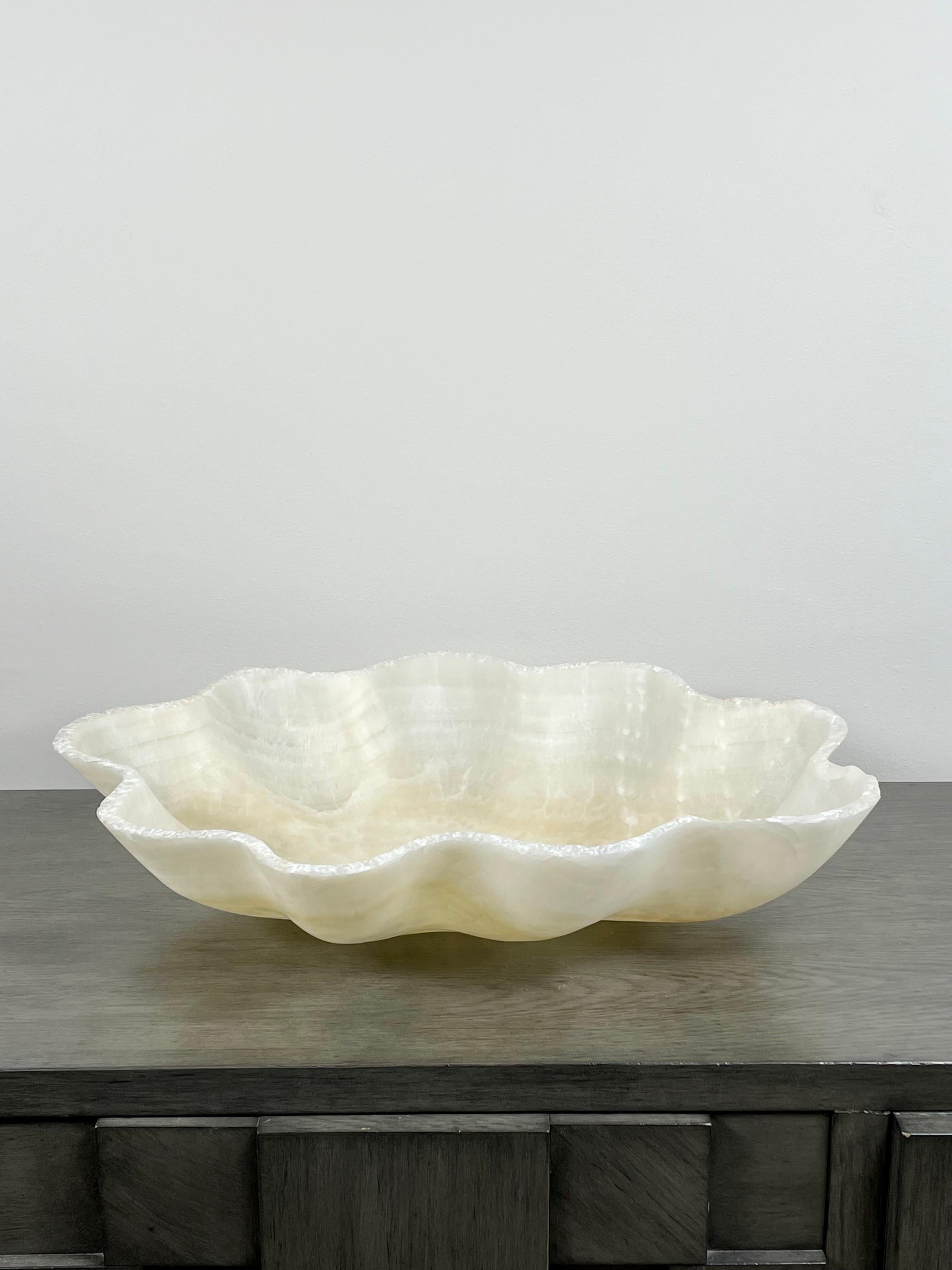 A stunning large scalloped shaped off-white onyx bowl with a raw edge. This one of a kind decorative bowl is meticulously hand-carved from a single piece of onyx by skilled artists to reveal its' inherent characteristics like the formation of layers