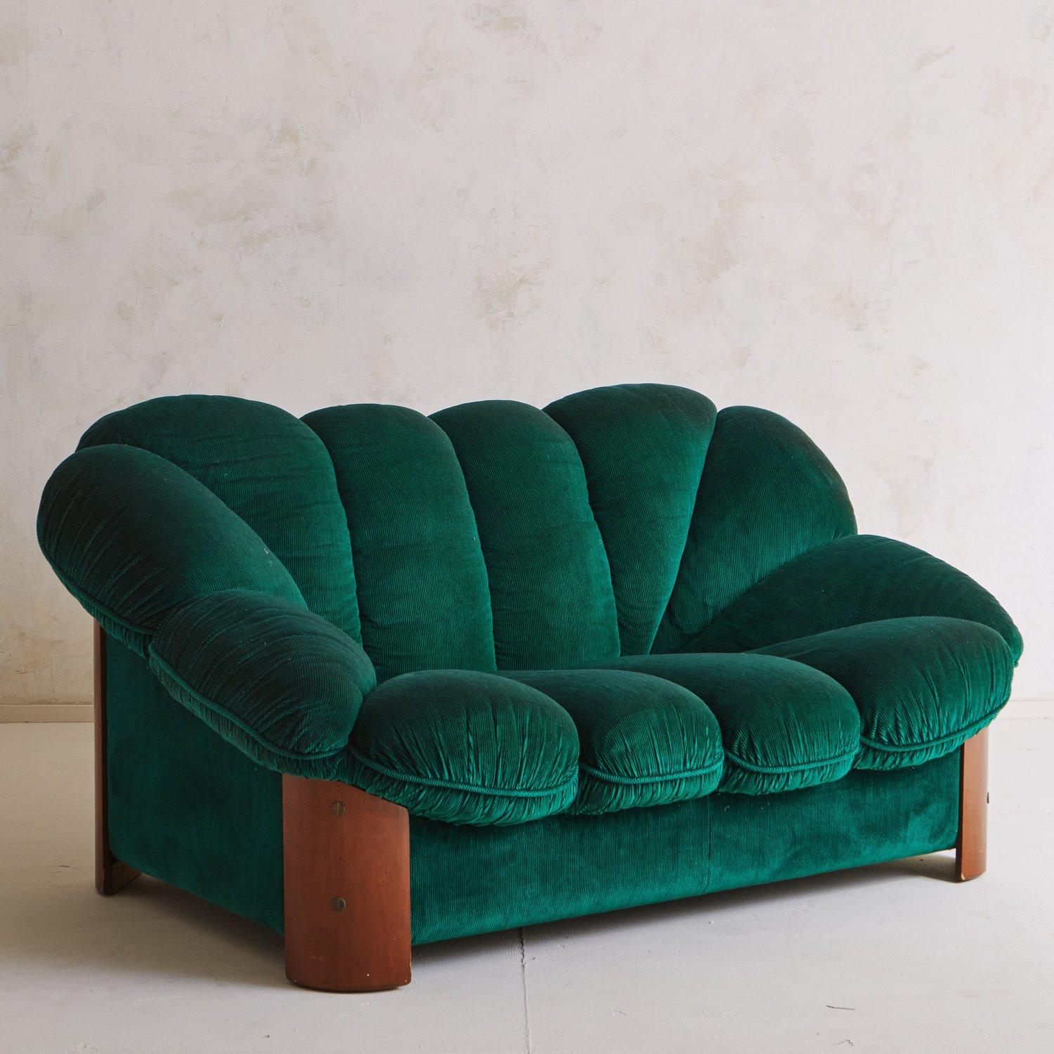 A vintage loveseat with a striking scalloped profile in original green velvet upholstery. This statement piece sits just off the ground on four curved cherry wood legs with sleek wood joinery. In the style of seating by designer Raphael Raffel.