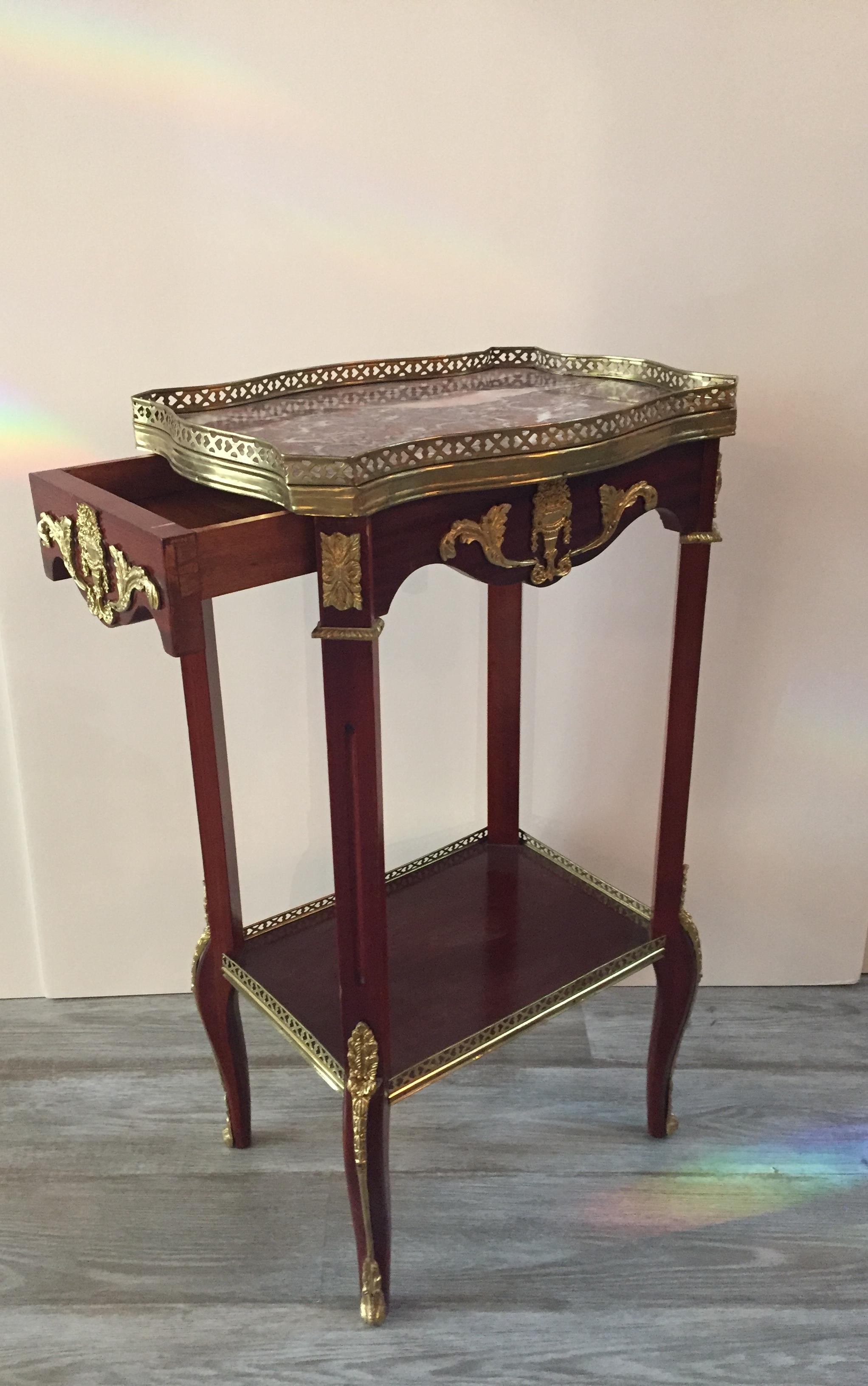 Louis XVI style fancy mahogany side table having ornate ormolu decoration , rouge and cream scalloped marble top with brass gallery, single drawer, lower tier with brass gallery and pretty feet that have cabriole shape.