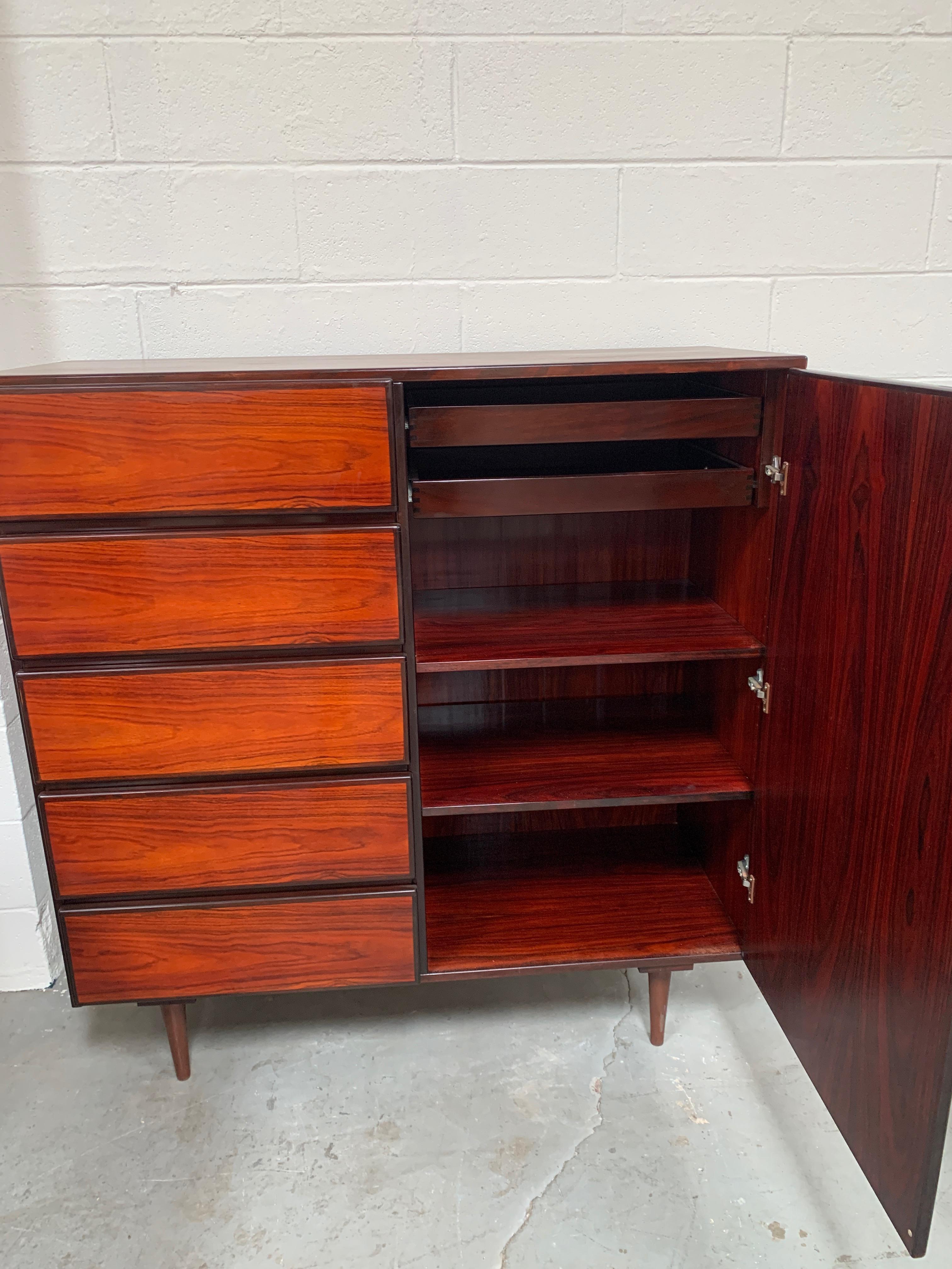 A tall wood storage cabinet stained in a deep red - signature of Scan Coll, made in Denmark. Complete with makers mark and quintessential midcentury pencil legs, this multipurpose cabinet can be used as a complement to its partner dresser or as a