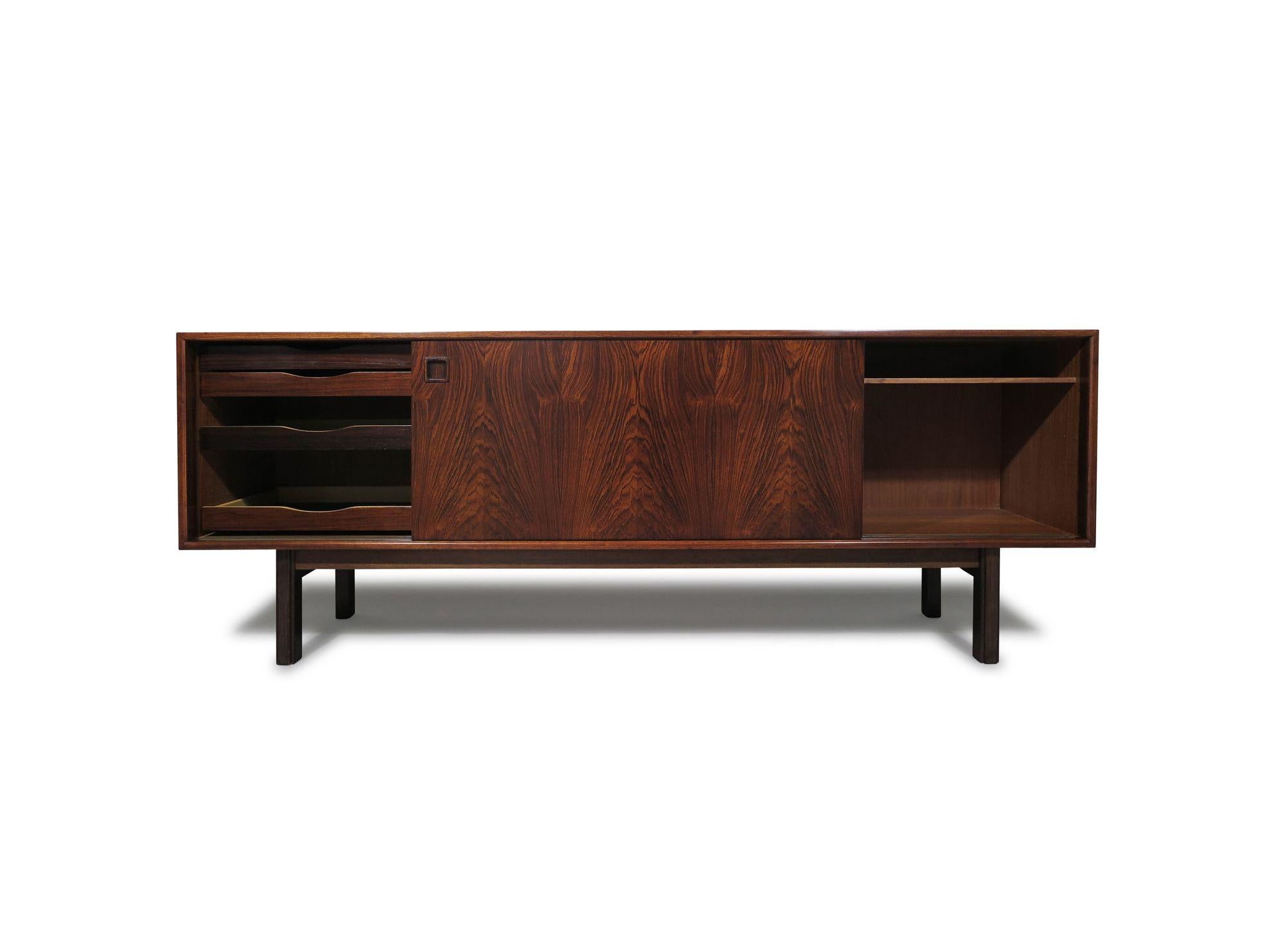 Mid-century Danish modern rosewood credenza designed and manufactured by cabinetmaker Omann Jun, Model 21, Denmark, circa 1960. This exquisite piece showcases rich colored Brazilian rosewood with a pair of sliding doors that reveal an interior with