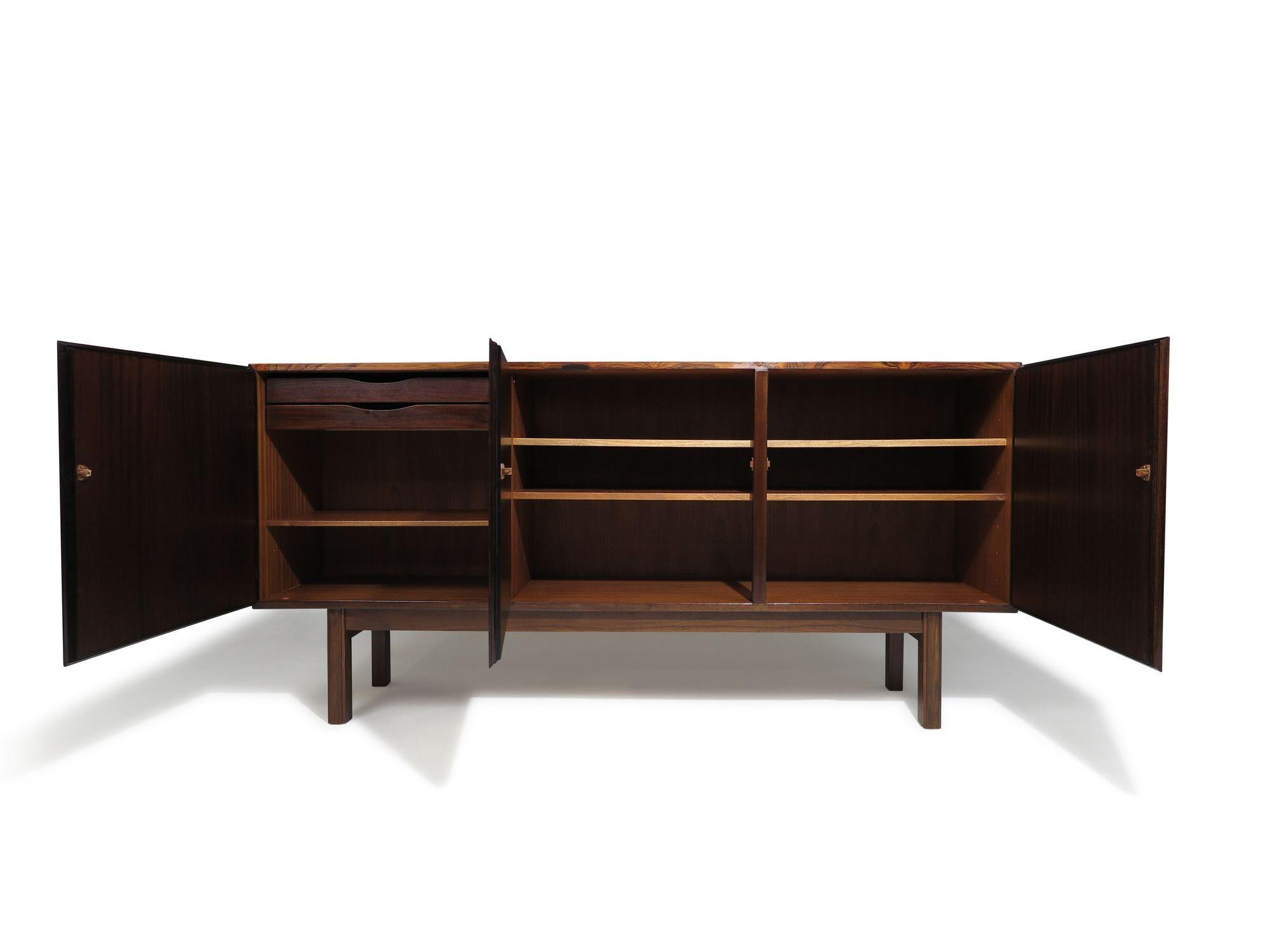 Mid-century Danish modern rosewood credenza designed and manufactured by cabinetmaker Omann Jun, Denmark, circa 1960.  Showcases richly colored Brazilian rosewood with a three minimal doors that reveal an interior with adjustable shelves and two
