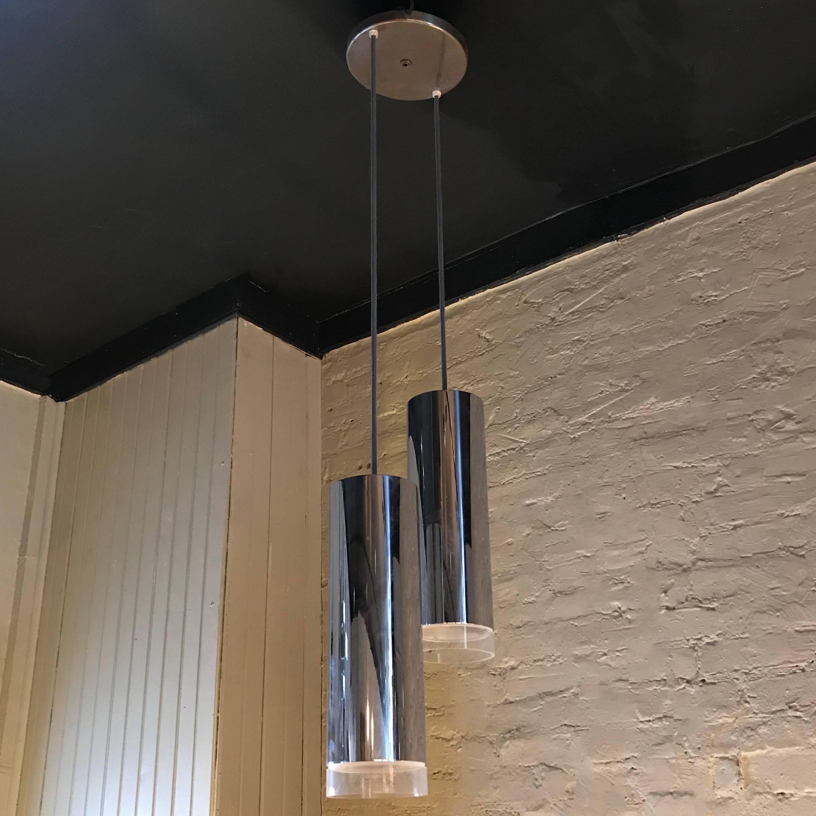 Striking, modernist pendant light, made in Switzerland, features two, graduated, chrome cylinders with Lucite trims hanging from a flat chrome disc. The cylinders each measure 15.25 inches height x 5 inches diameter.