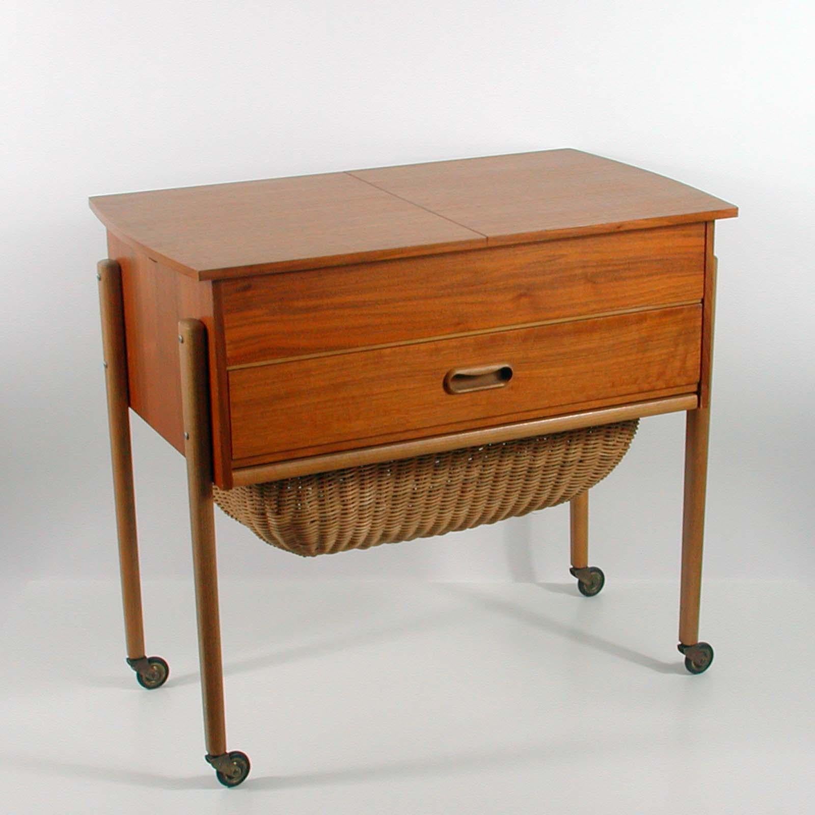 This awesome sewing box or cabinet was designed and manufactured in Denmark in the 1950s to 1960s.

The sewing table has got one drawer and a built in pull out basket underneath. The two top pieces slide apart. It is made of teak with birch