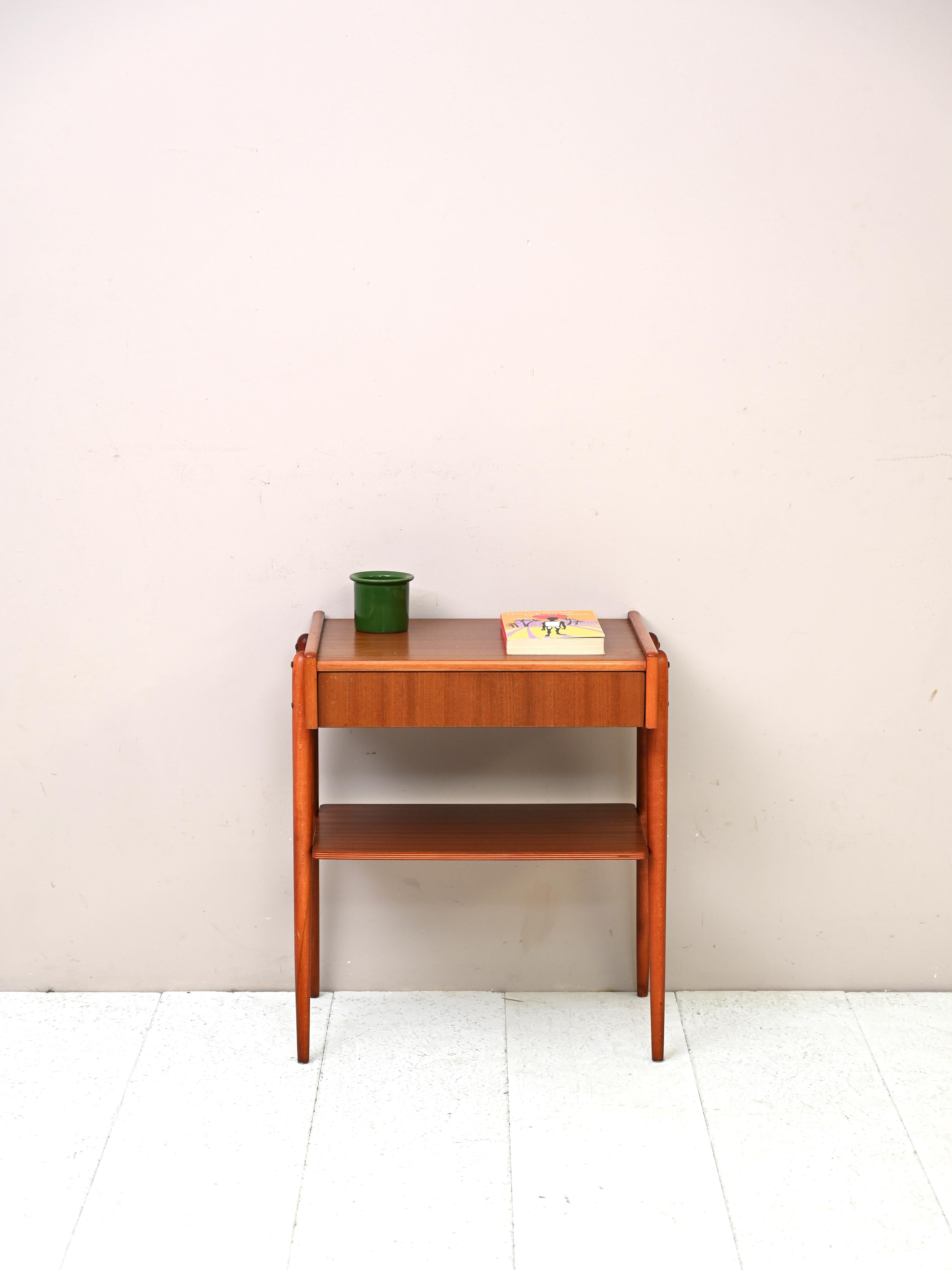 Mahogany bedside table with drawer built into the frame.
A piece of furniture with an original mid-century Nordic design. The teak wood frame is linear and uncluttered but enhanced by the concealed drawer and long tapered legs. There is also a teak