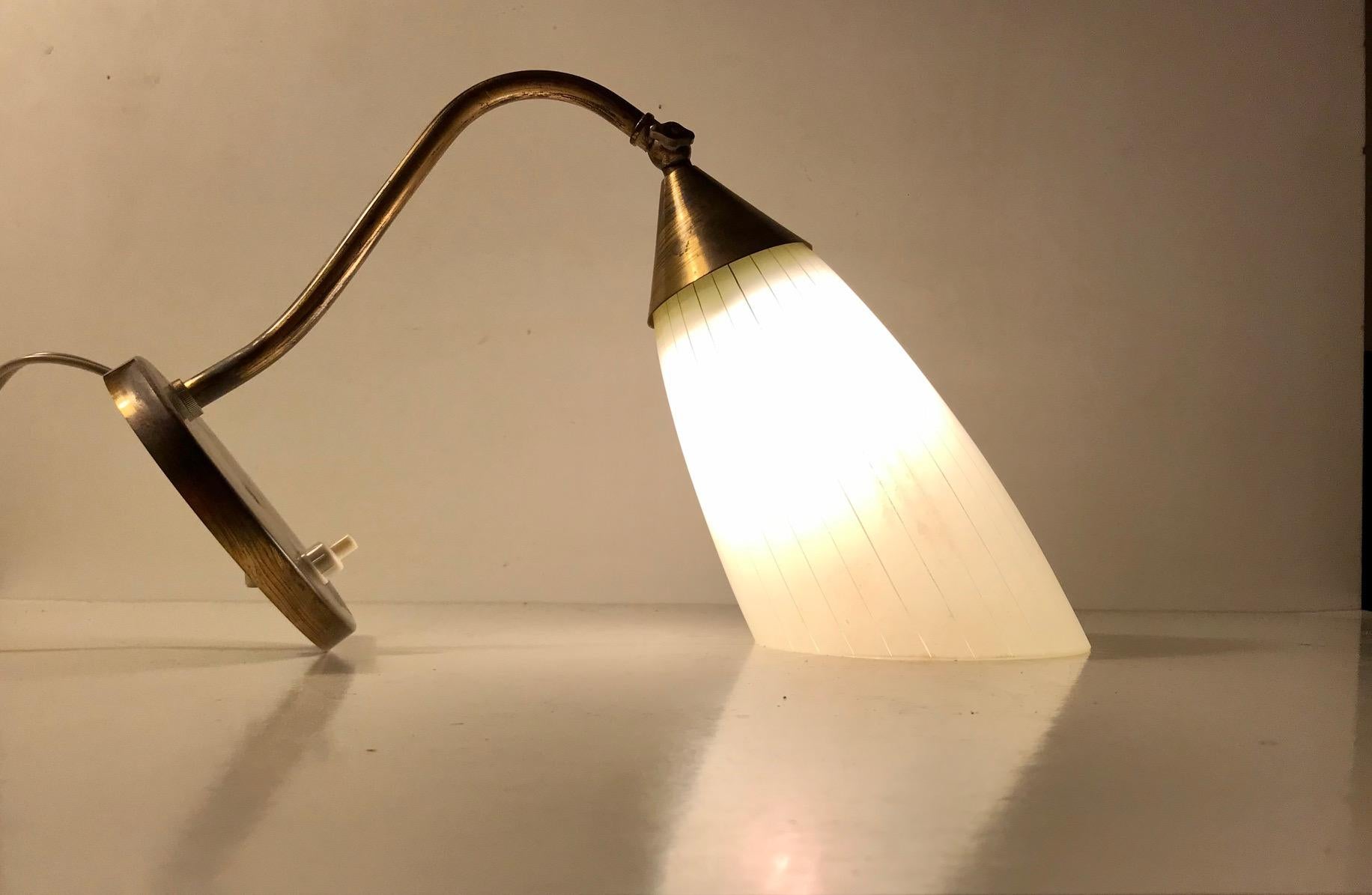 Early 1950s wall light made in Scandinavia in a style reminiscent of Stilnovo and the french modernist movement. Its composed of patinated brass and mounted with an angle-cut white pinstriped glass shade. Its adjustable by the shade up/down and side