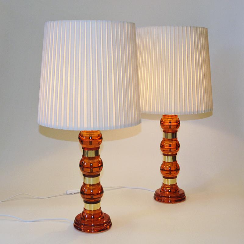 Lovely amber colored Scandinavian pair of art glass table lamps from the 1960s. Sectioned with transparent amber colored balls on top of each other,  separeted with brass details in between. Elegant shape string of pearls design. 
Great together or