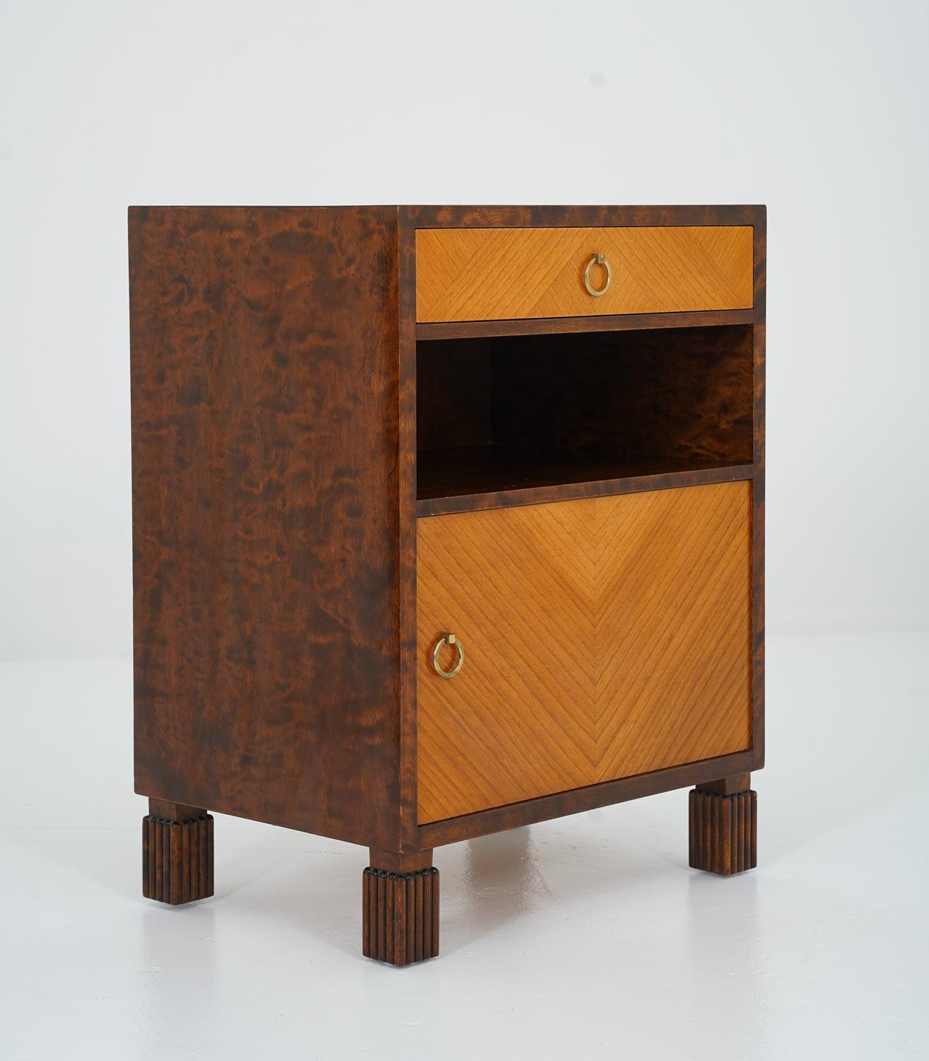 A pair of rare art deco bedside tables manufactured by Bodafors, Sweden, 1940s. 
The body of the tables is veneered in dark-stained birch, while the front is veneered with elm, with its grain creating a beautiful pattern. The round brass details