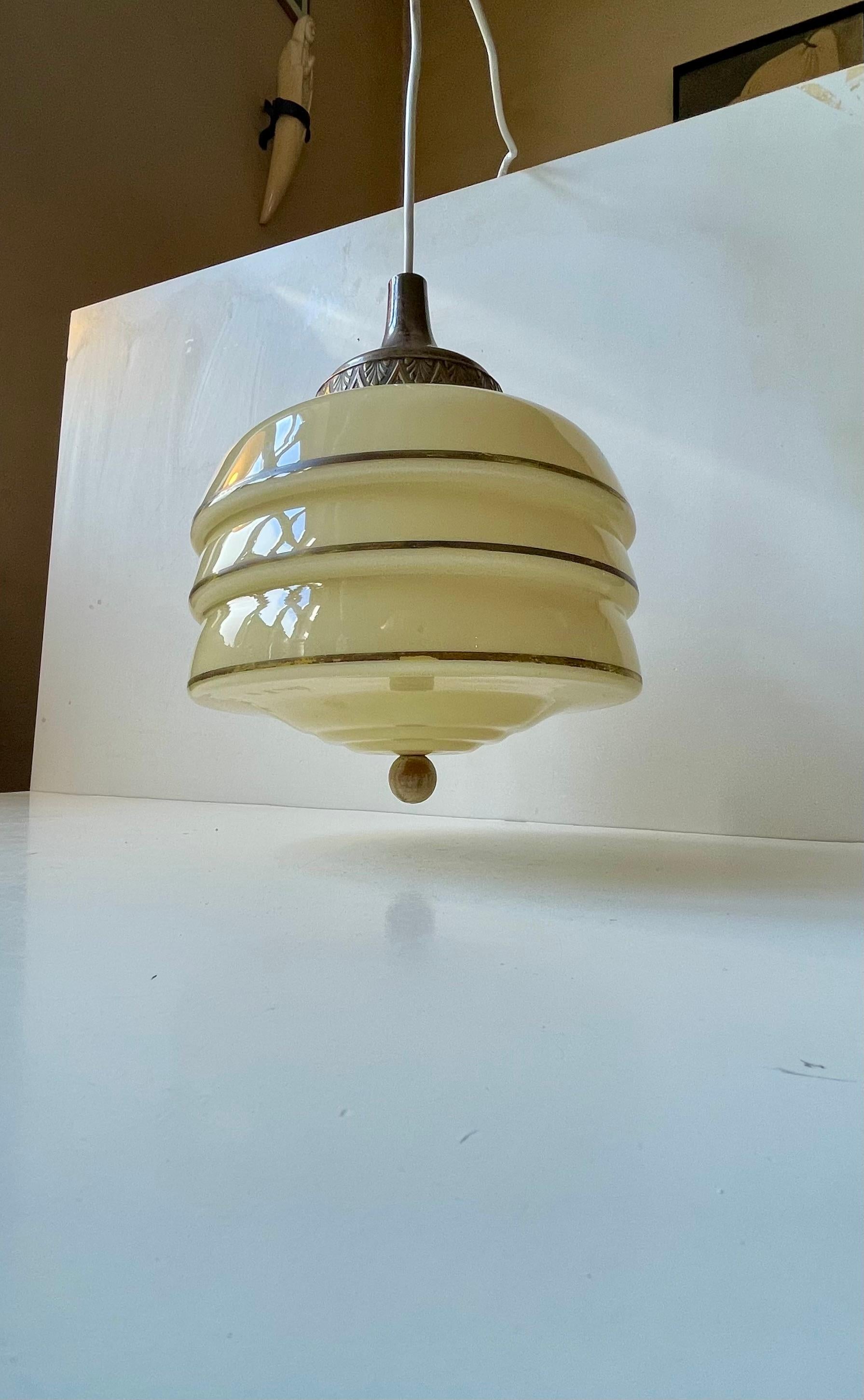 Art Deco hanging pendant light featuring a beehive shaped shade in light yellow/beige partially striped opaline glass, a suspended wooden sphere at the bottom and a top in partially silver-plated brass. Made in Scandinavia during the 1930s. 3 meters